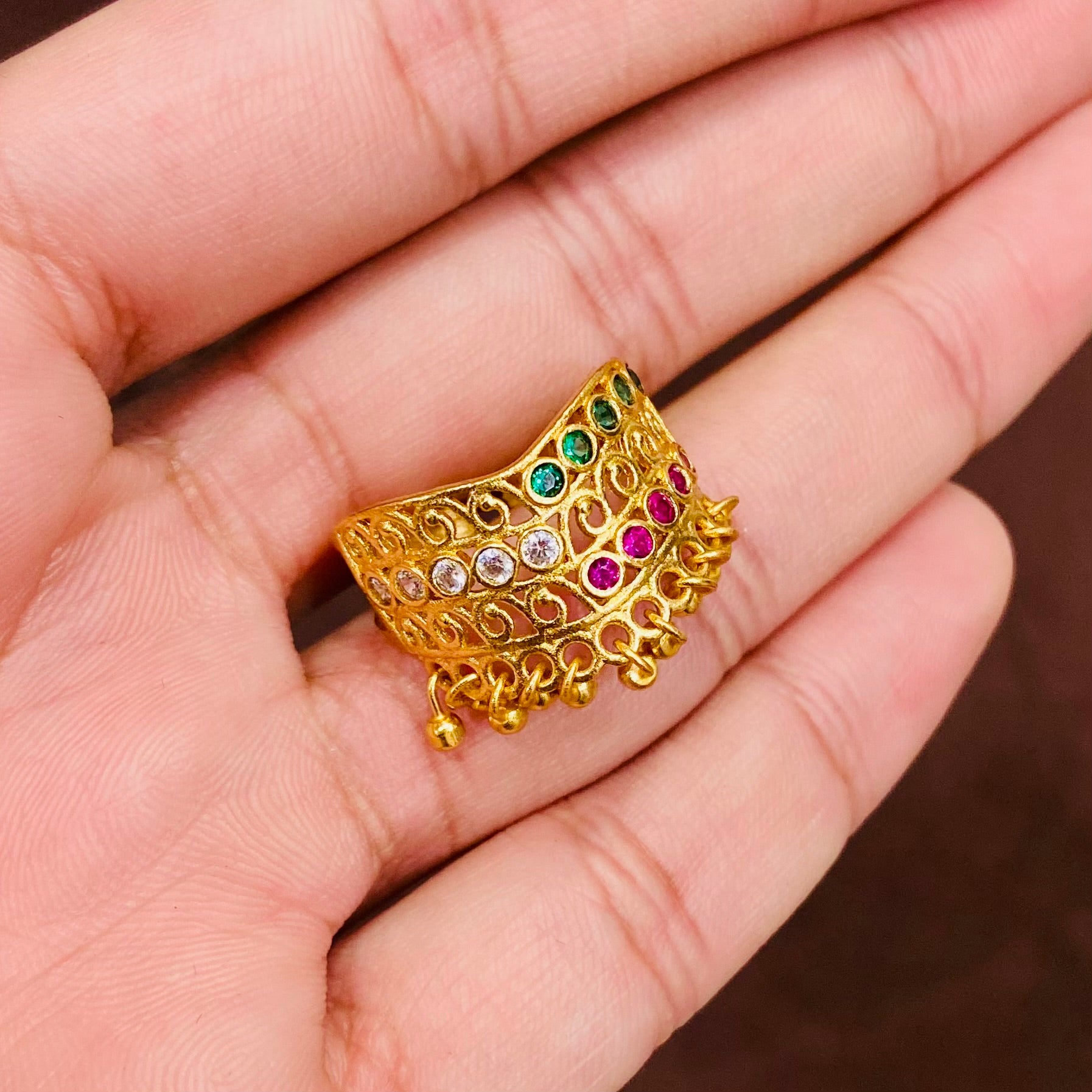 Gold jewelry piece with gemstones held in a hand against a neutral background