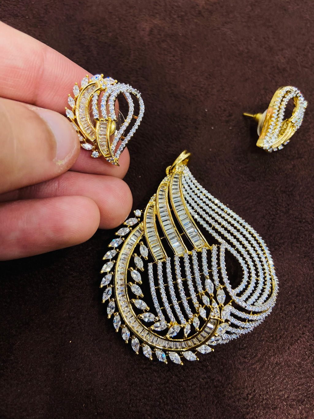 Gold and diamond earrings on a brown surface with a hand holding one earring.