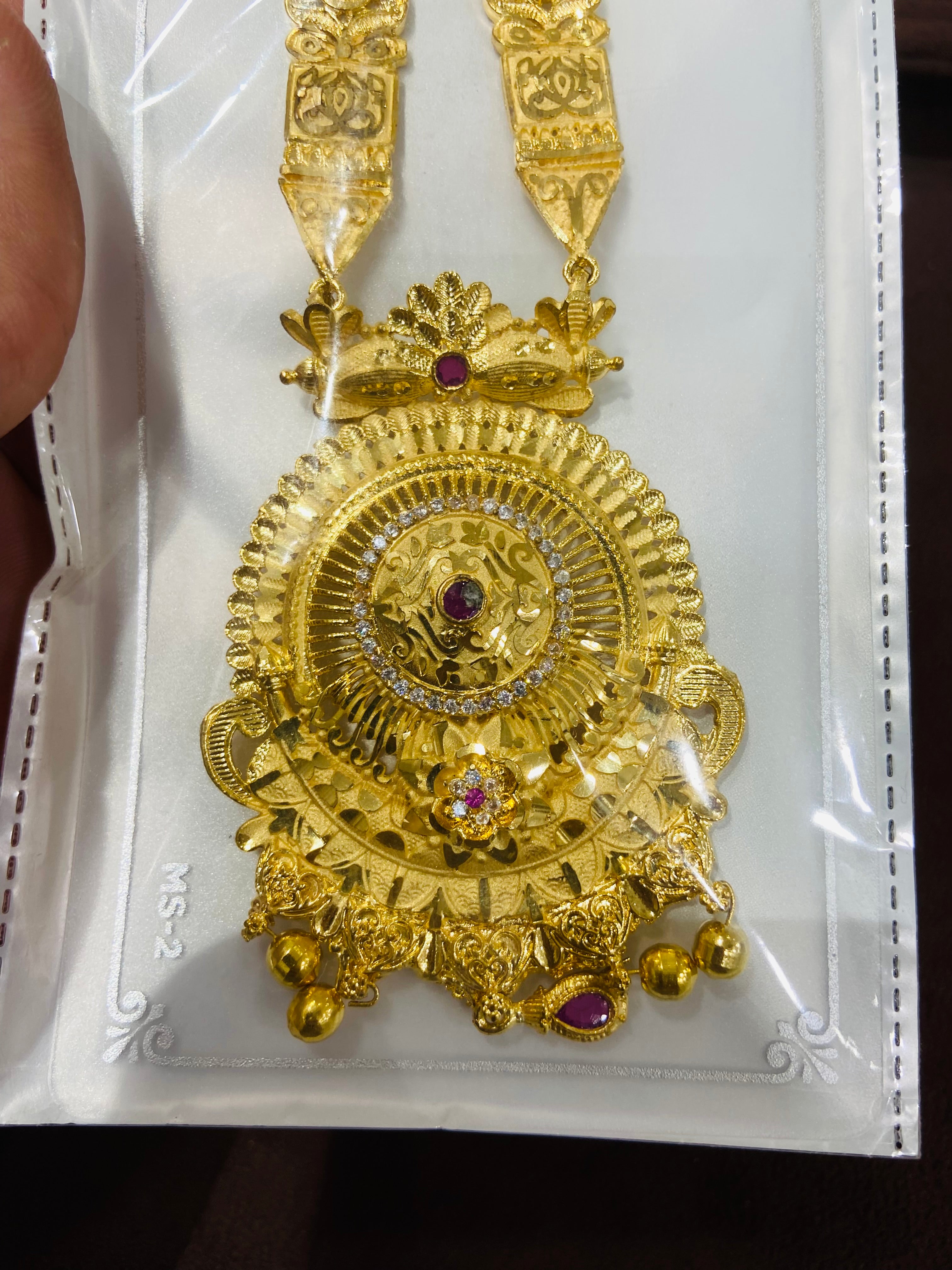 Gold necklace with intricate design and red gemstones on a white card