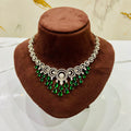 Necklace with green gemstones on a brown velvet stand against a marble background