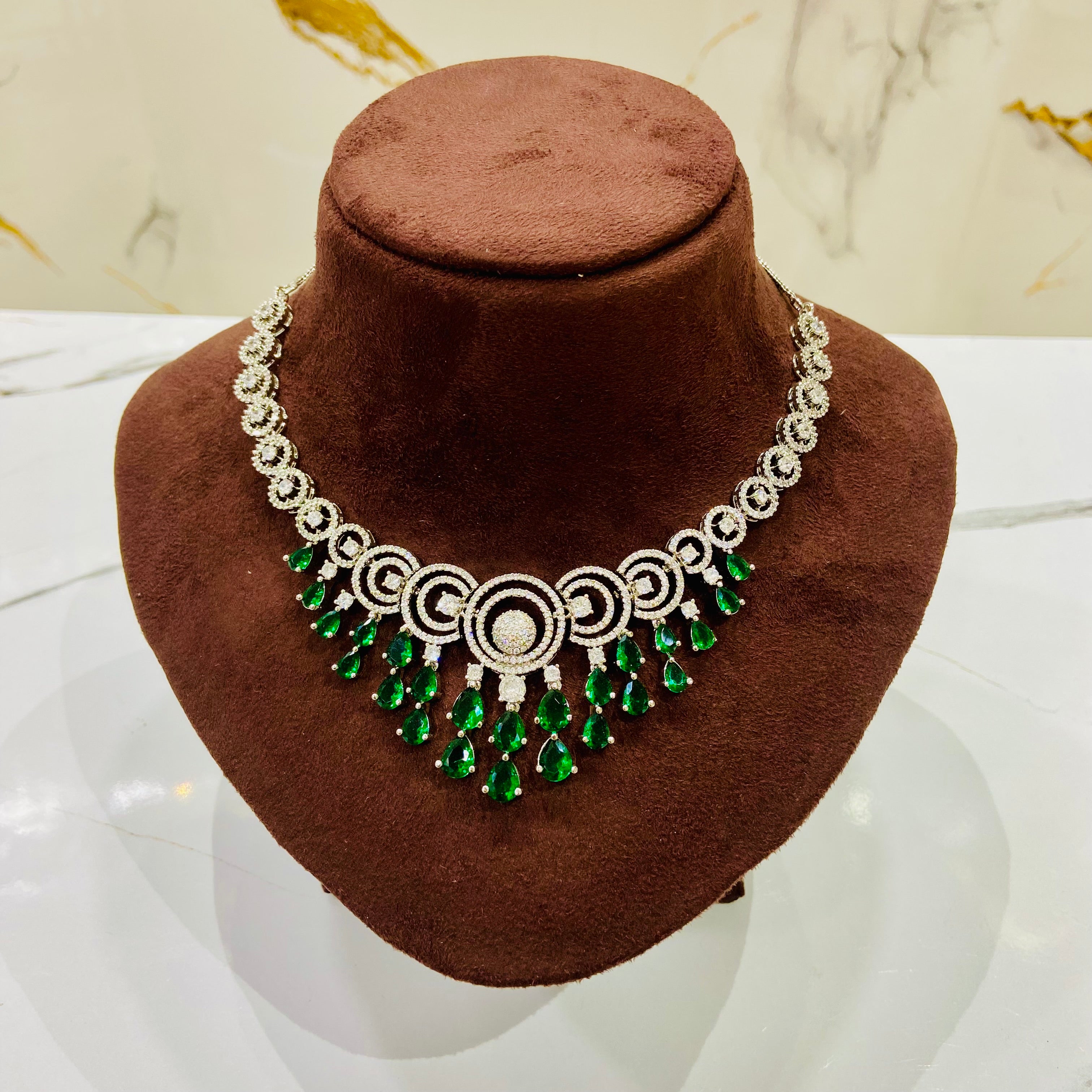 Necklace with green gemstones on a brown velvet stand against a marble background