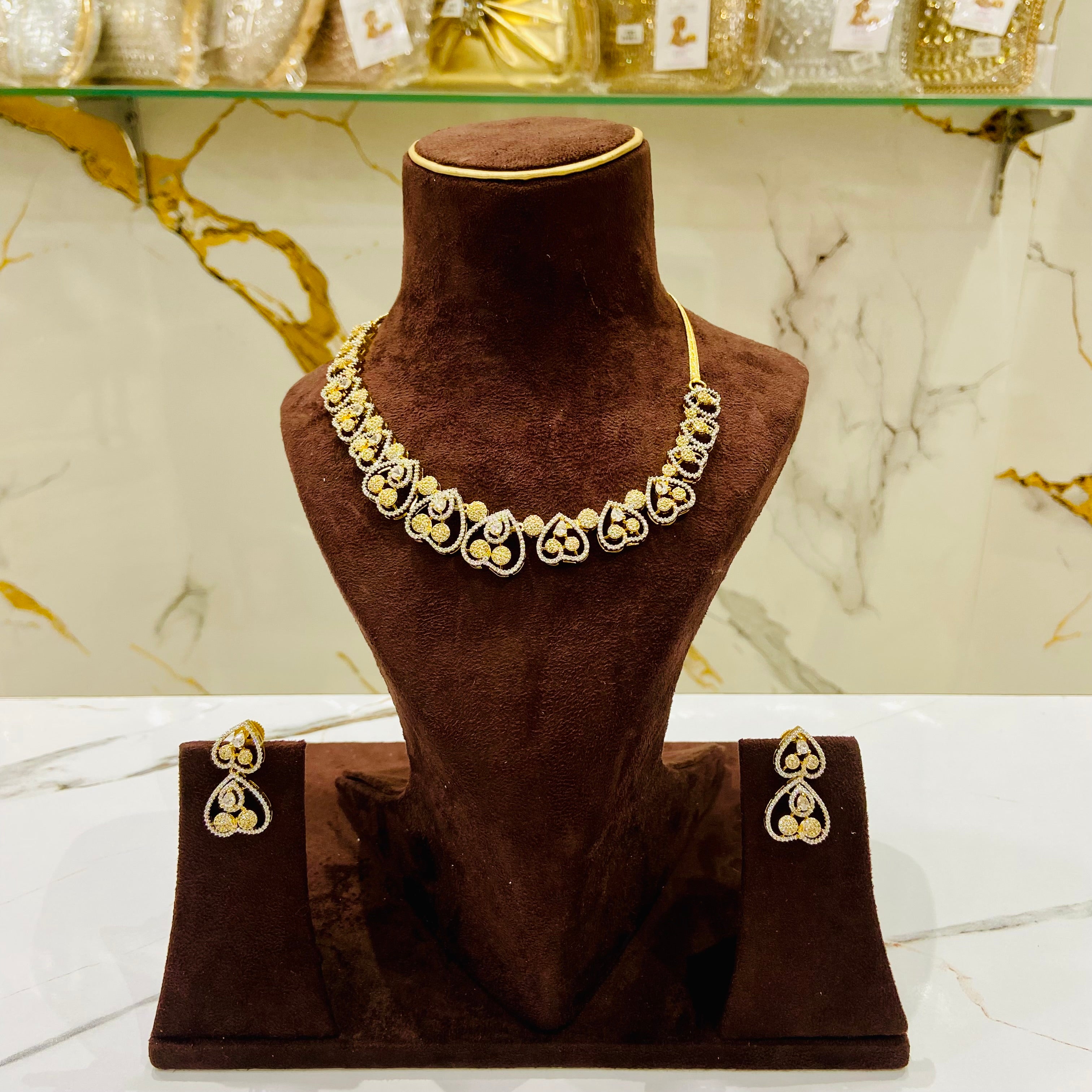 Gold necklace and earrings on a brown mannequin bust with a marble background