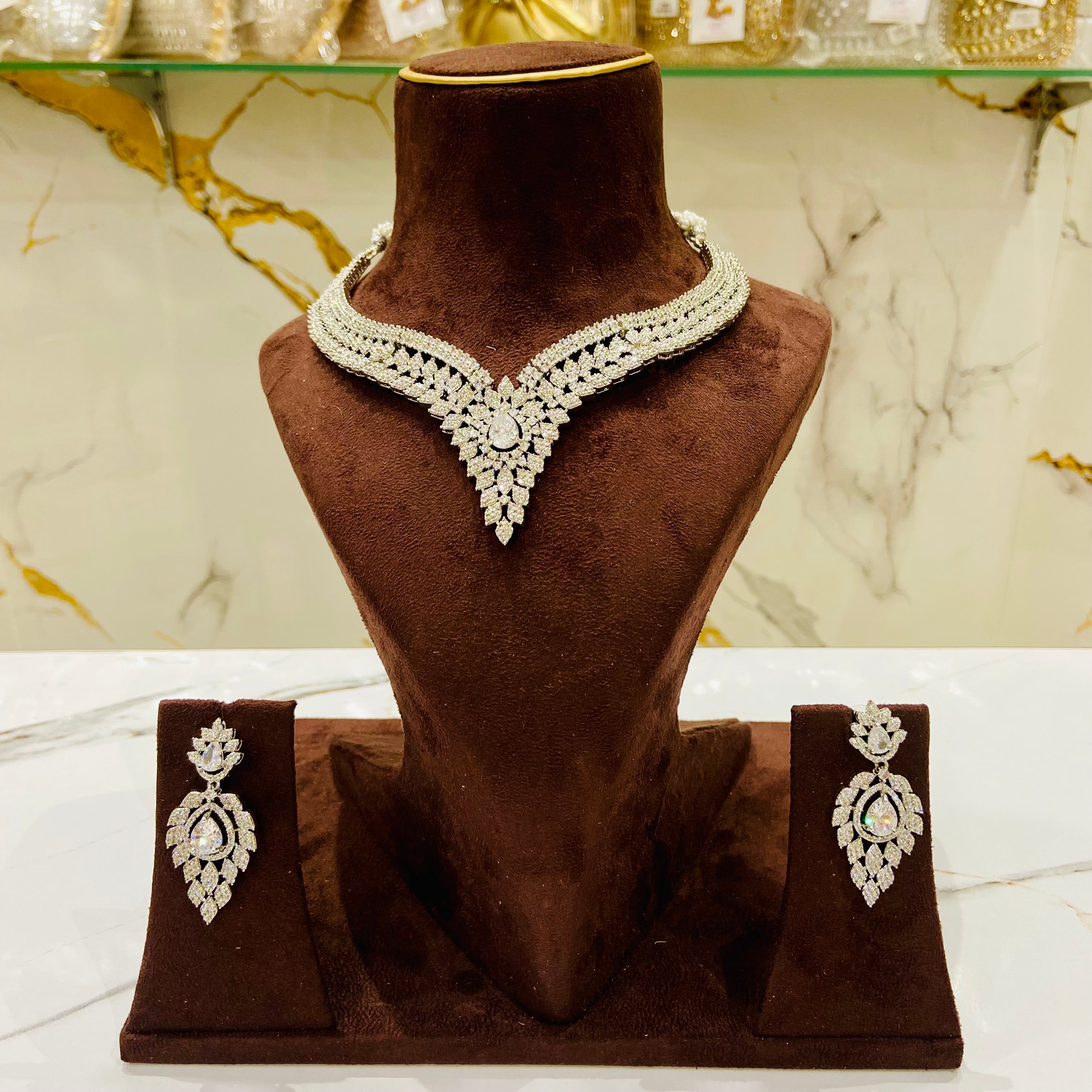 Jewelry set with necklace and earrings on a brown velvet stand against a marble background