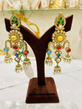 Pair of ornate earrings with colorful gemstones on a brown velvet stand.