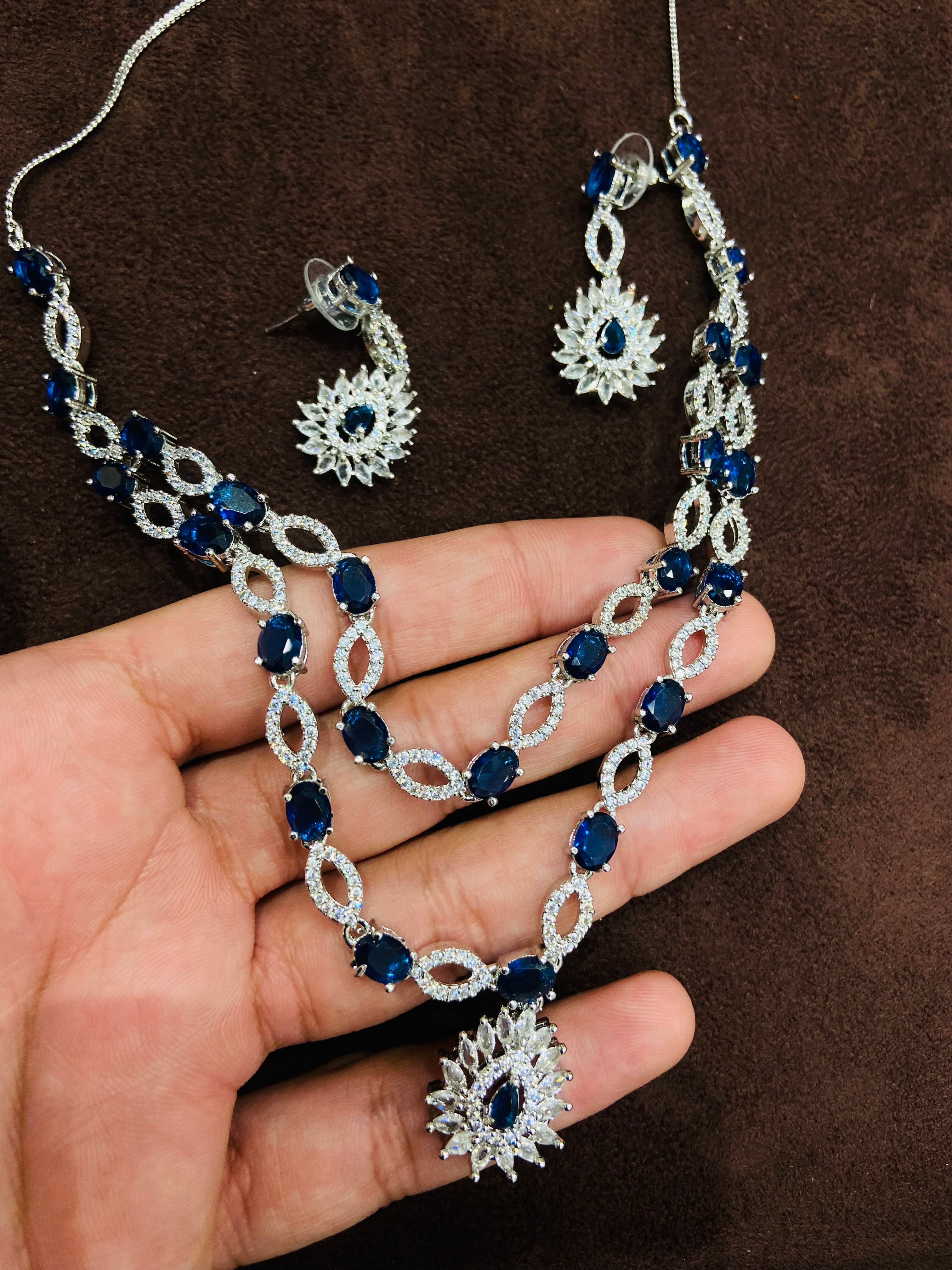 Silver necklace with blue stones held by a hand on a brown background