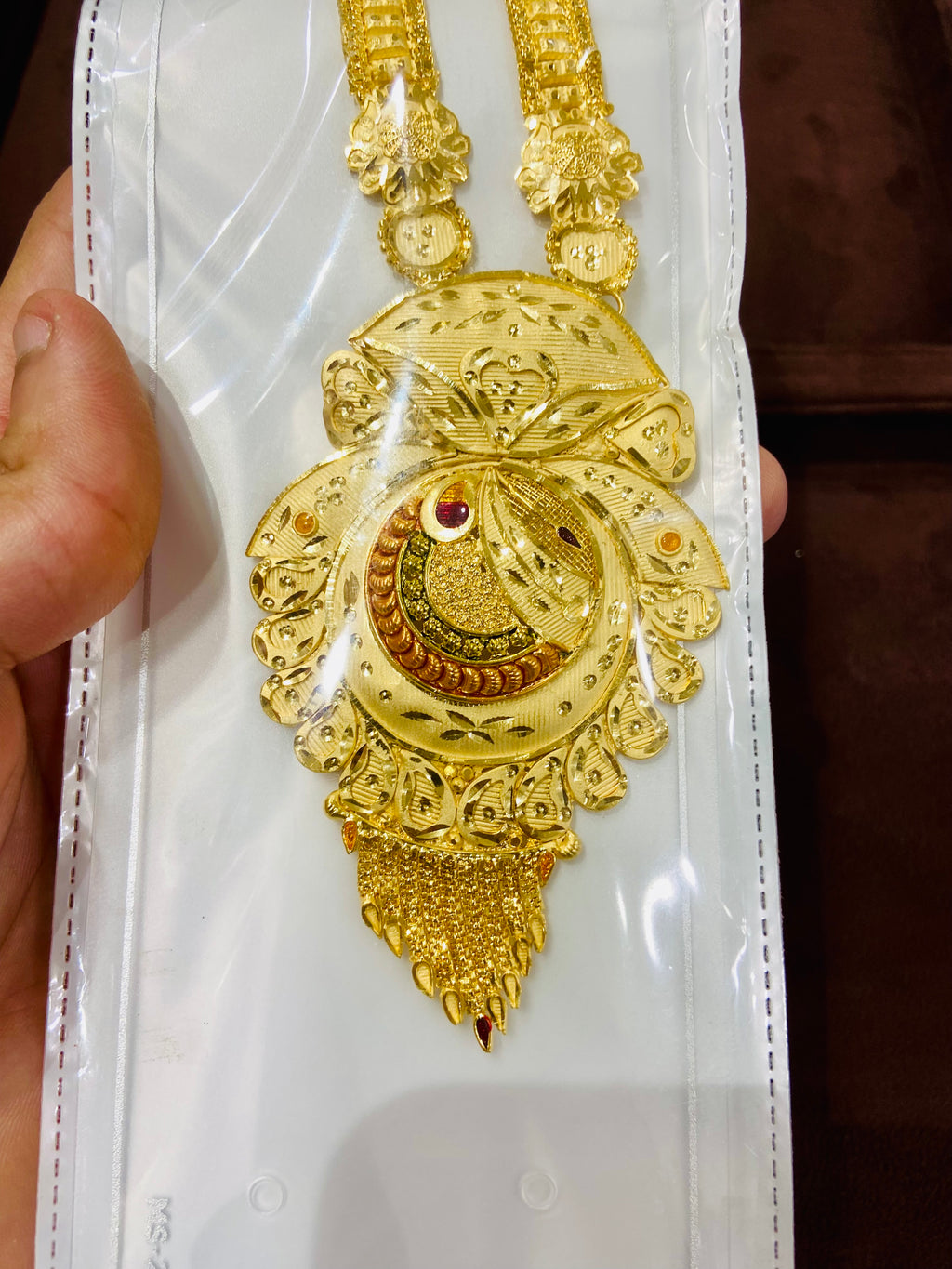 Gold necklace with intricate design held by a hand on a white background