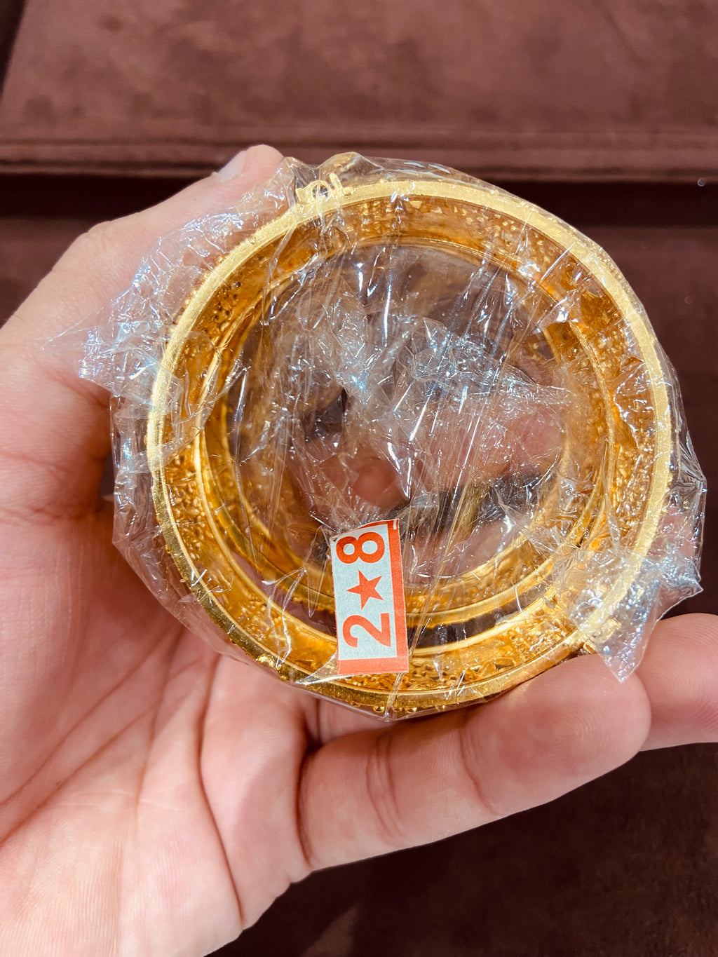 Gold circular object with plastic wrap held in a hand against a brown background