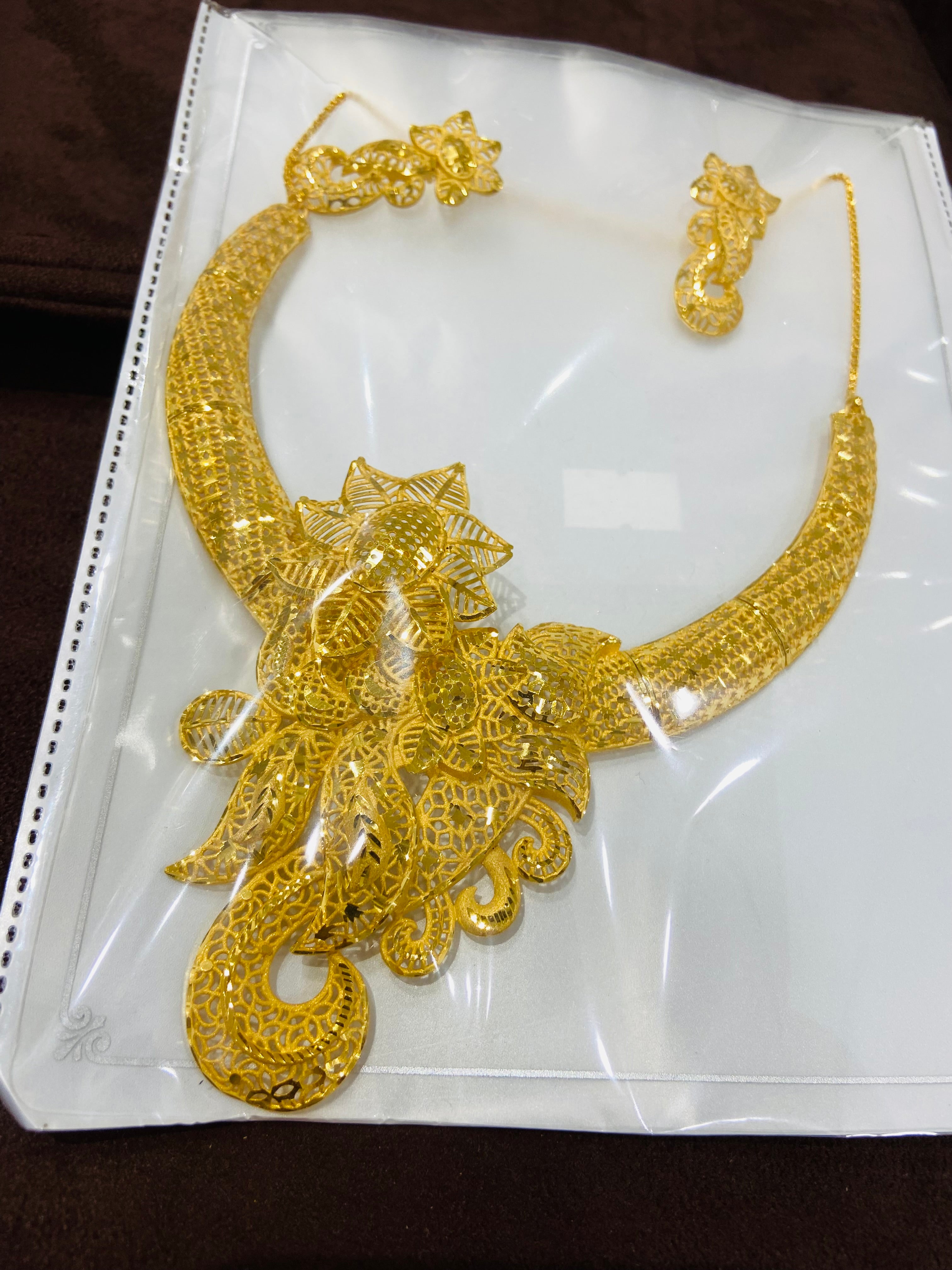 Gold necklace and earrings set in clear packaging on a white background