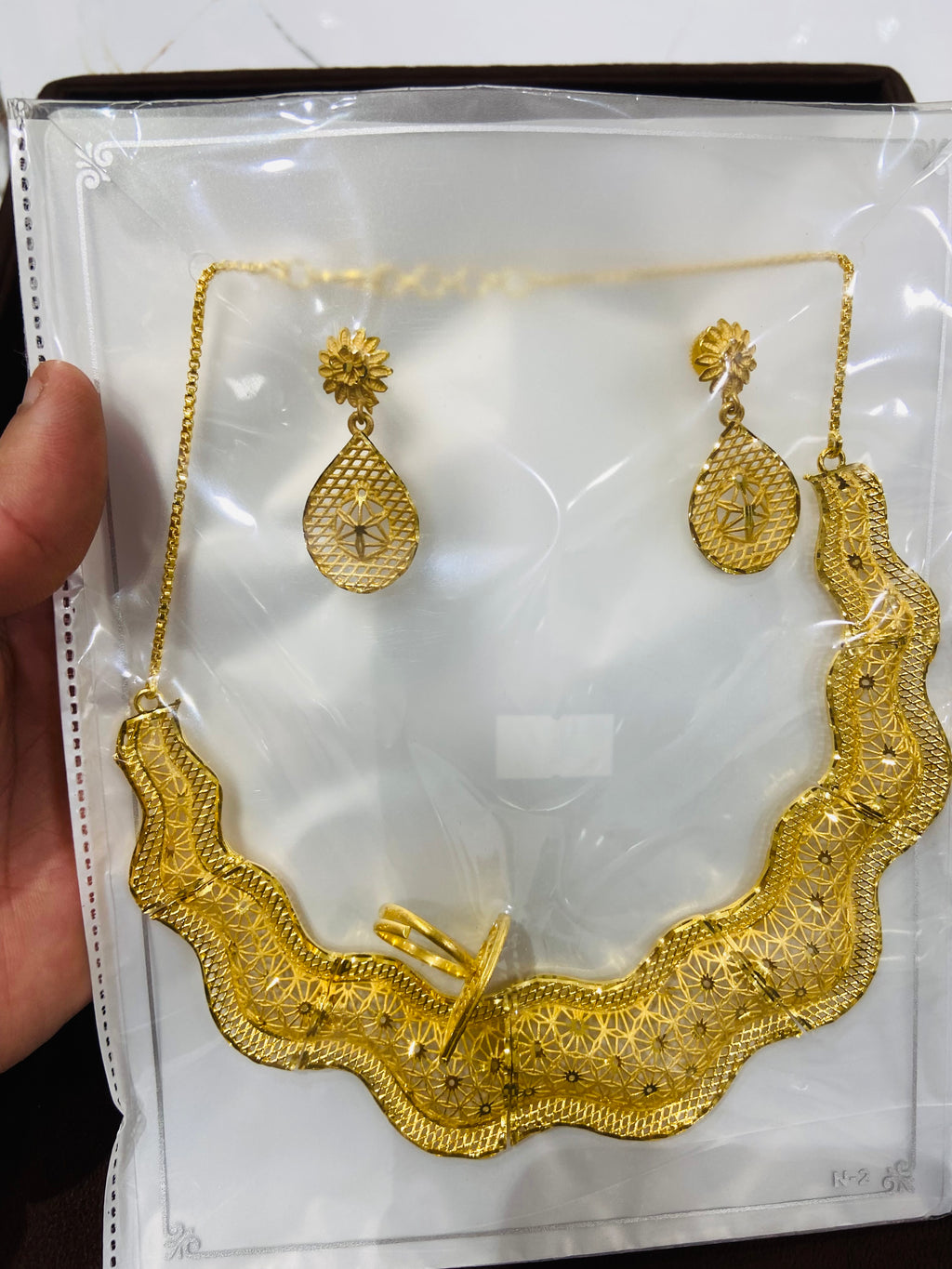 Gold necklace and earrings on a white card held by a hand.