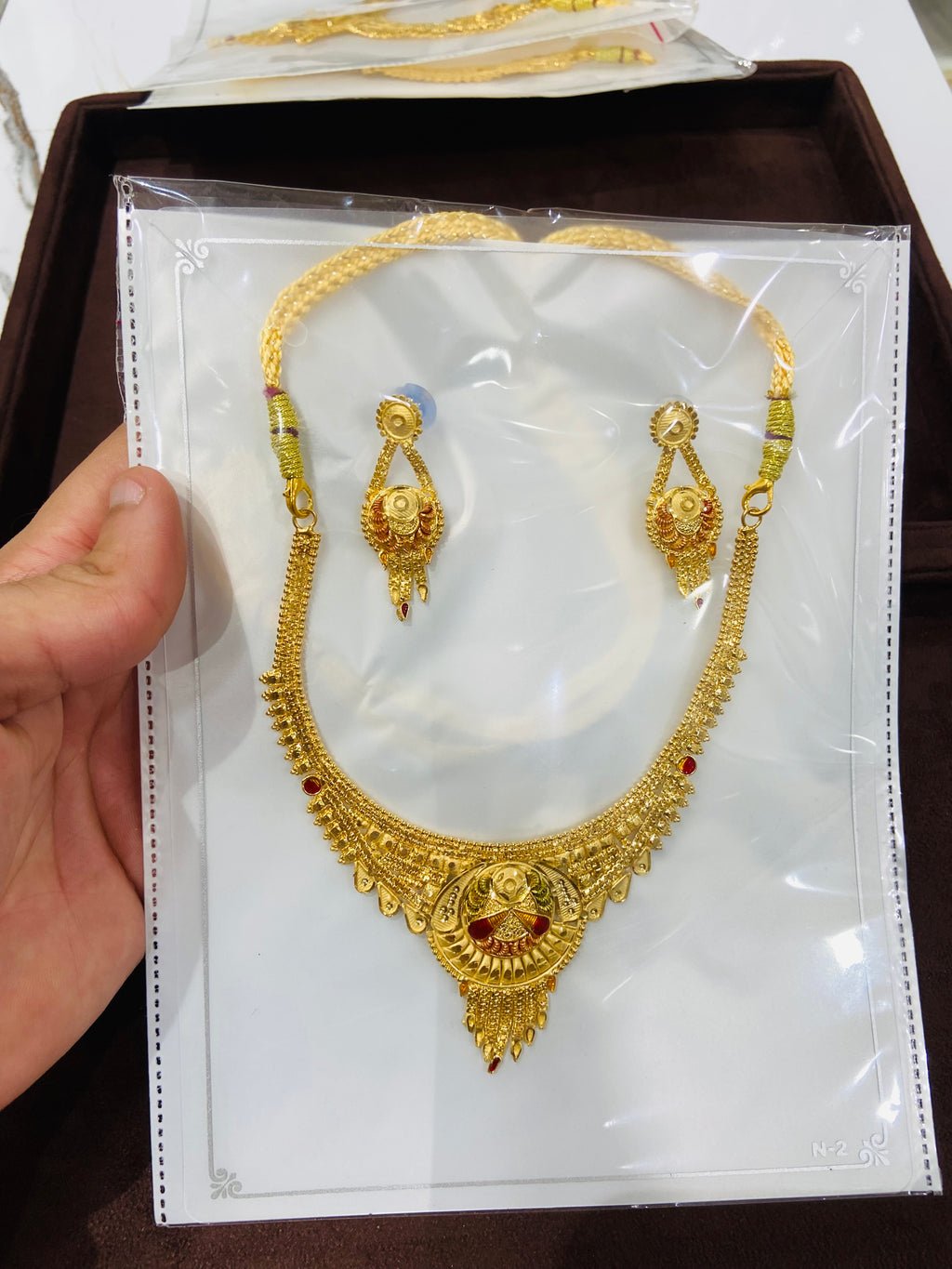 Gold necklace and earrings set on a card held by a hand