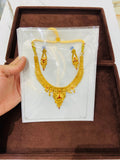 Gold necklace and earrings on a white card held by a hand, with a brown box in the background.