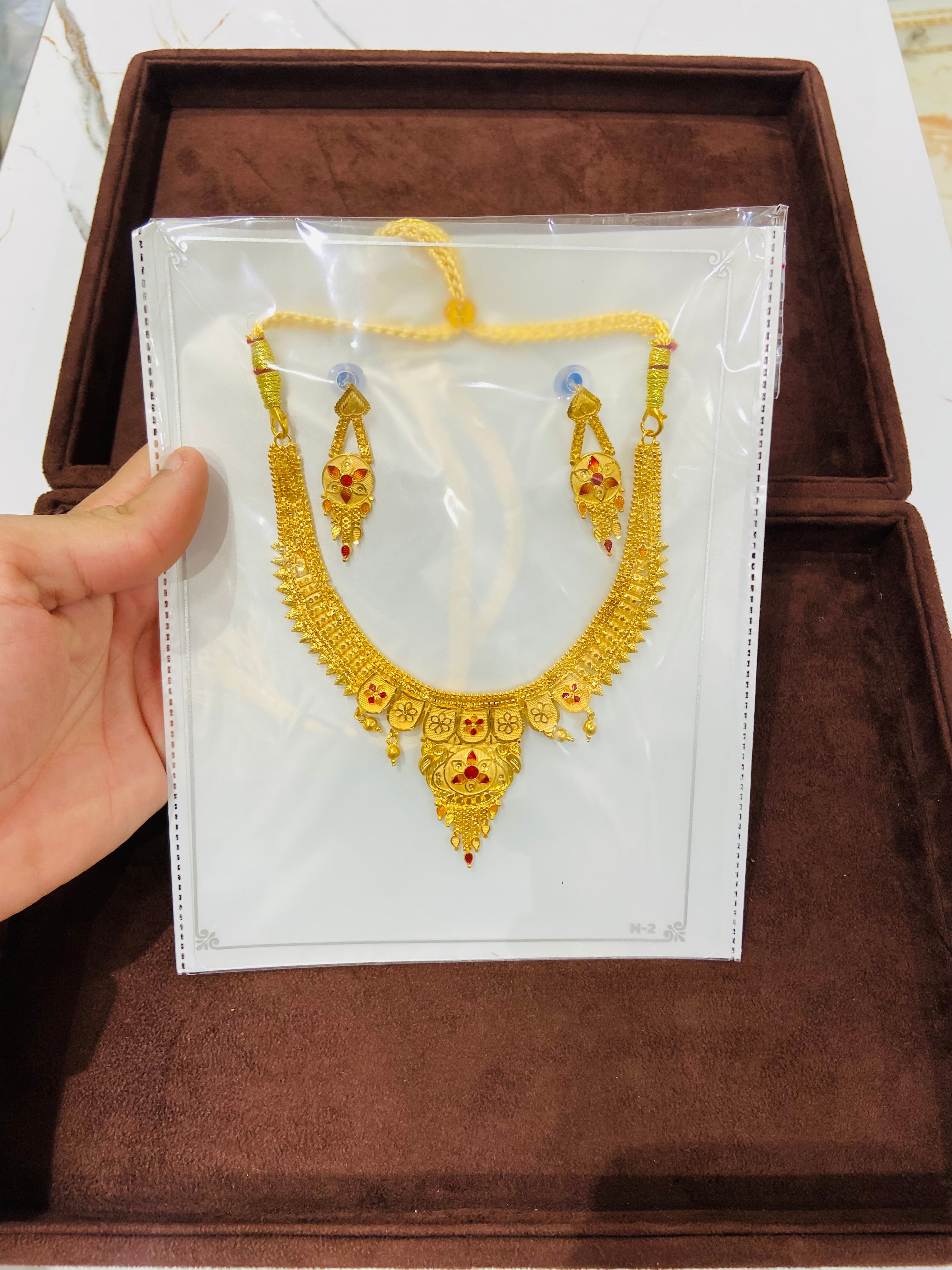 Gold necklace and earrings on a white card held by a hand, with a brown box in the background.