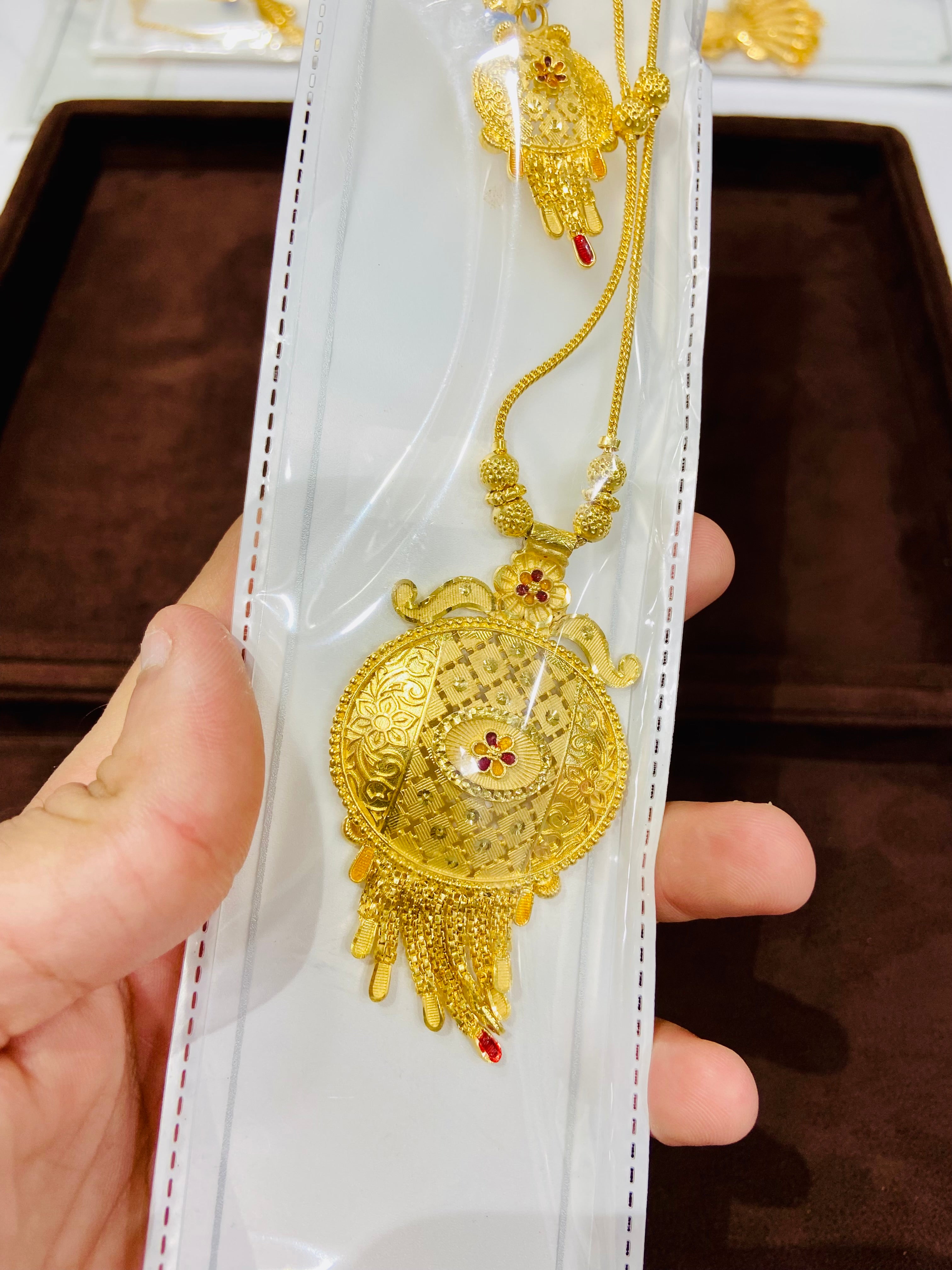 Gold necklace with intricate design held by a hand against a dark background