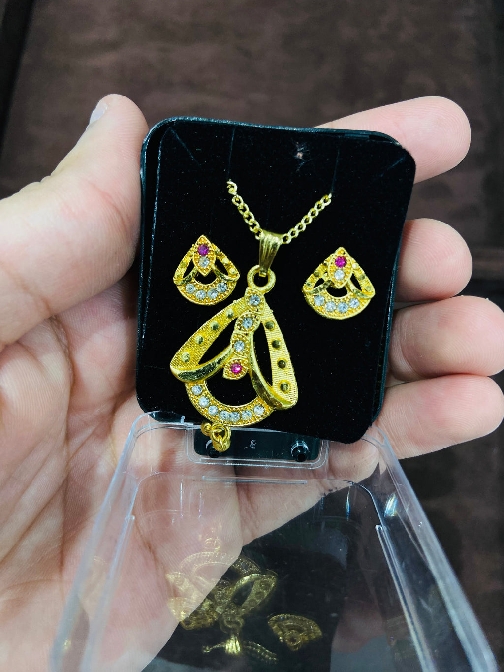 Gold jewelry set with gemstones on a black display card held by a hand.
