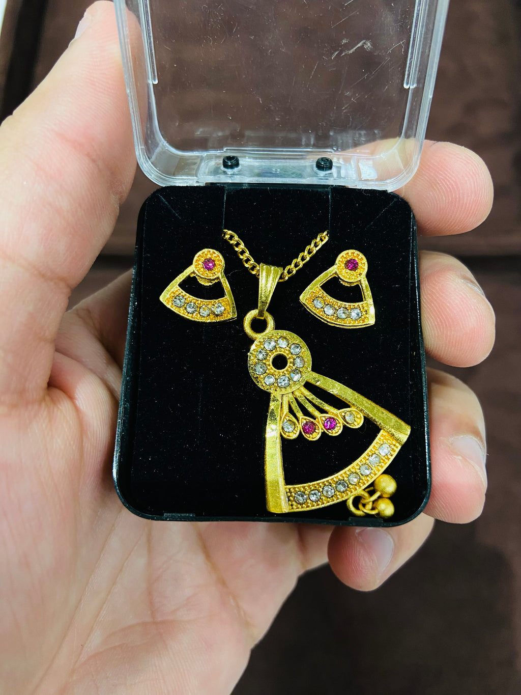Gold heart-shaped earrings with red gemstones on a black display card held by a hand.