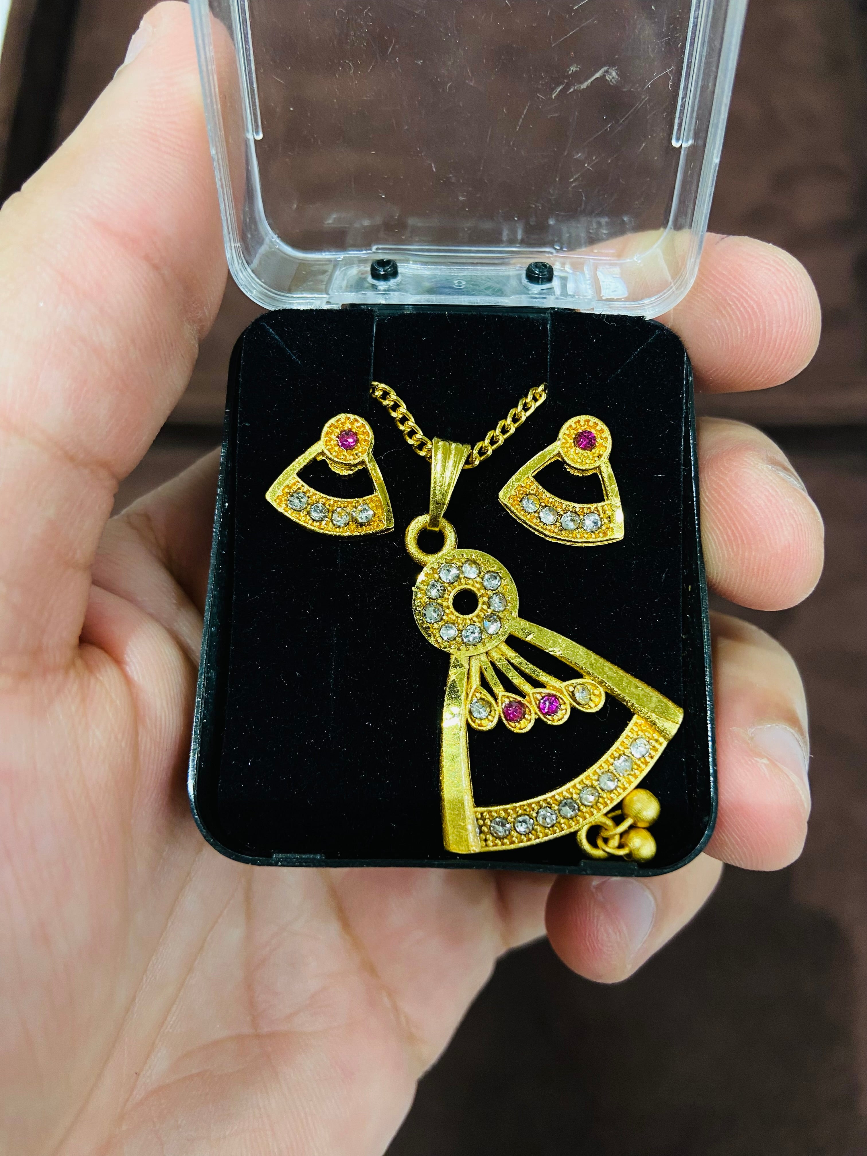 Gold heart-shaped earrings with red gemstones on a black display card held by a hand.