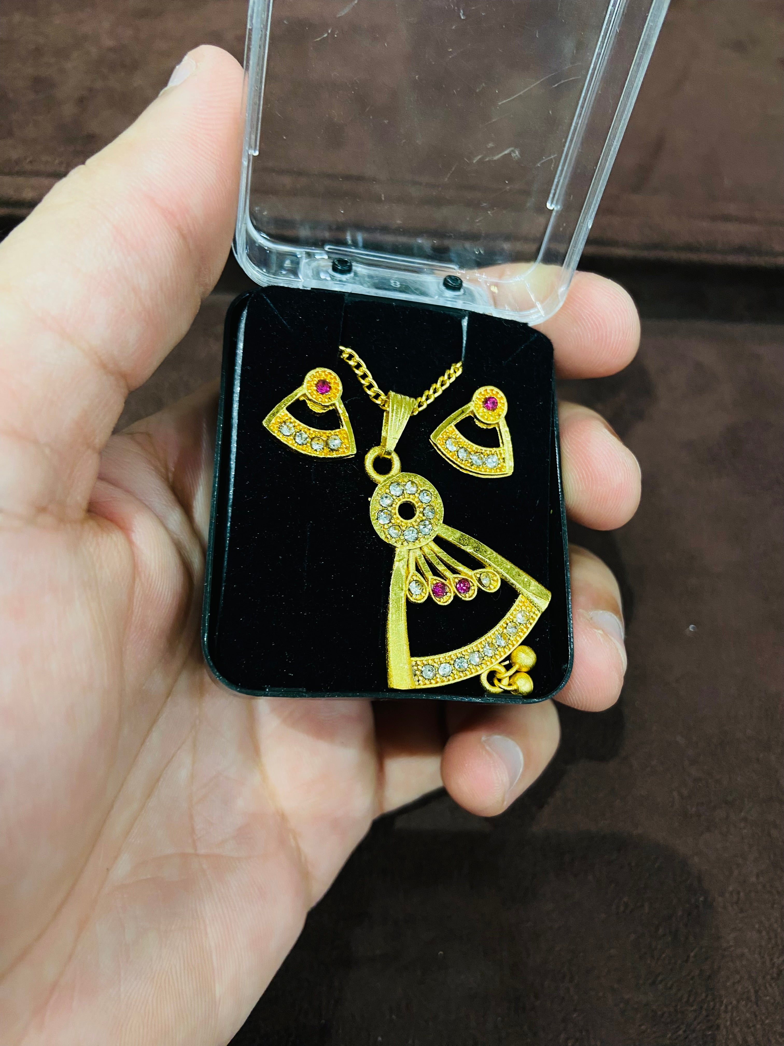 Gold heart-shaped earrings with red stones in a clear case held by a hand.