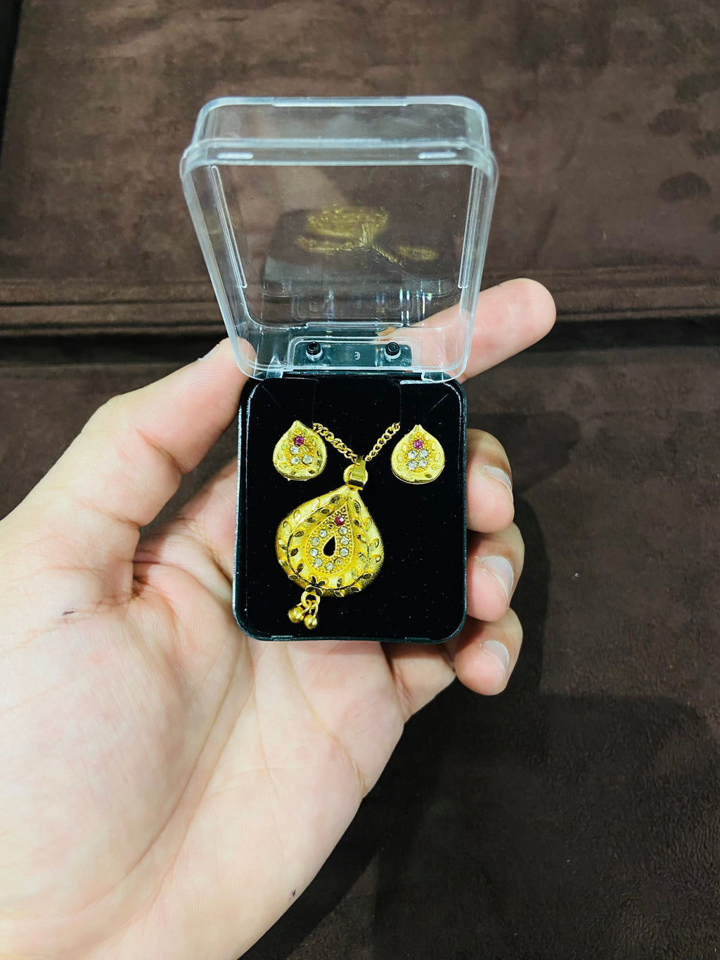 Gold earrings in a clear jewelry box held by a hand on a dark background