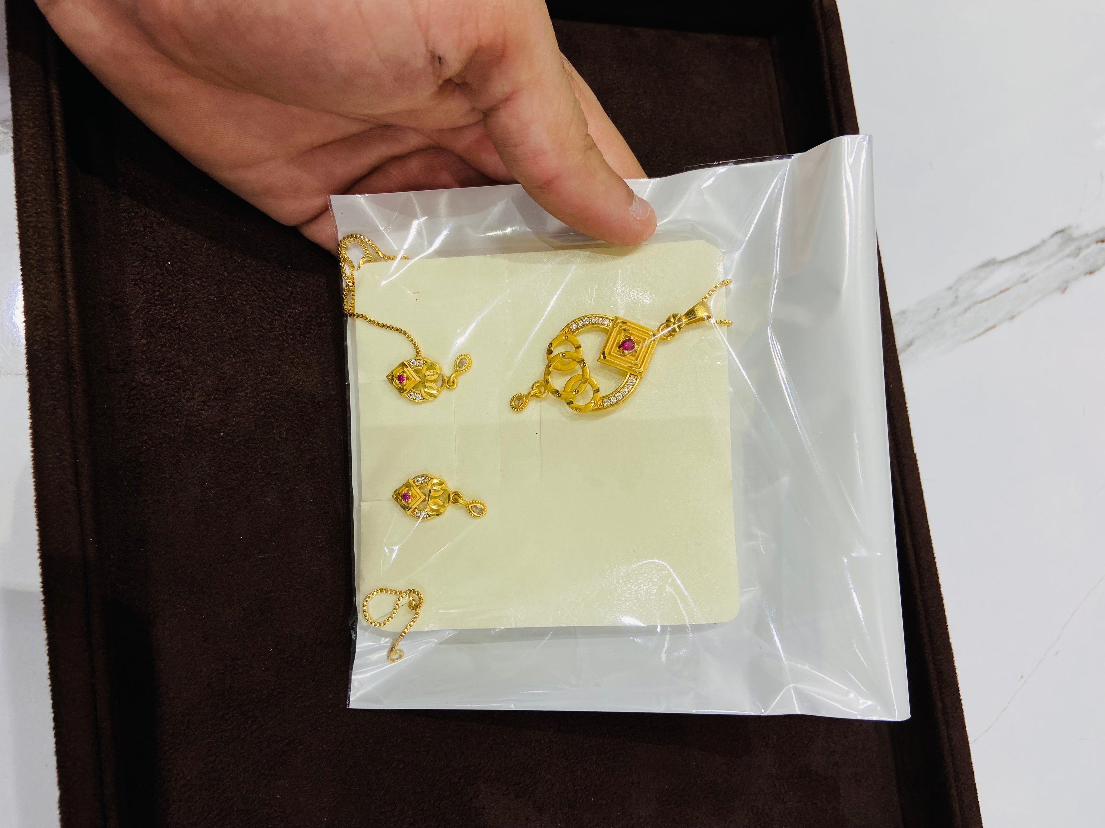 Gold necklace on a white card held by a hand with a brown background