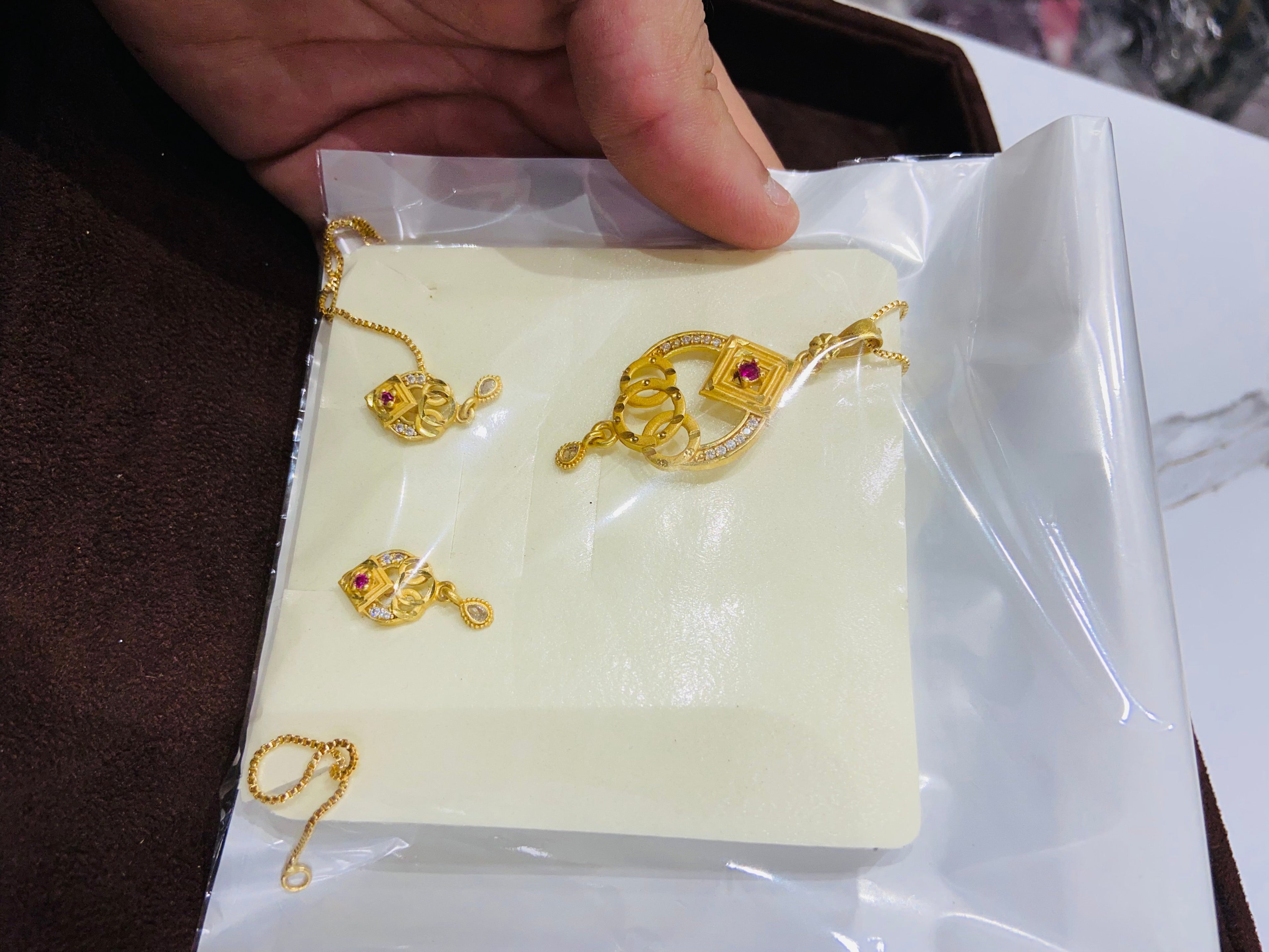Gold jewelry set on a white card with a hand holding it