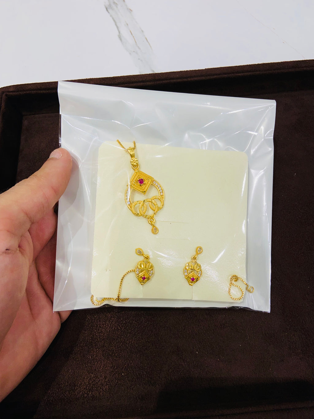 Gold jewelry set on a white cloth with a hand holding the package.