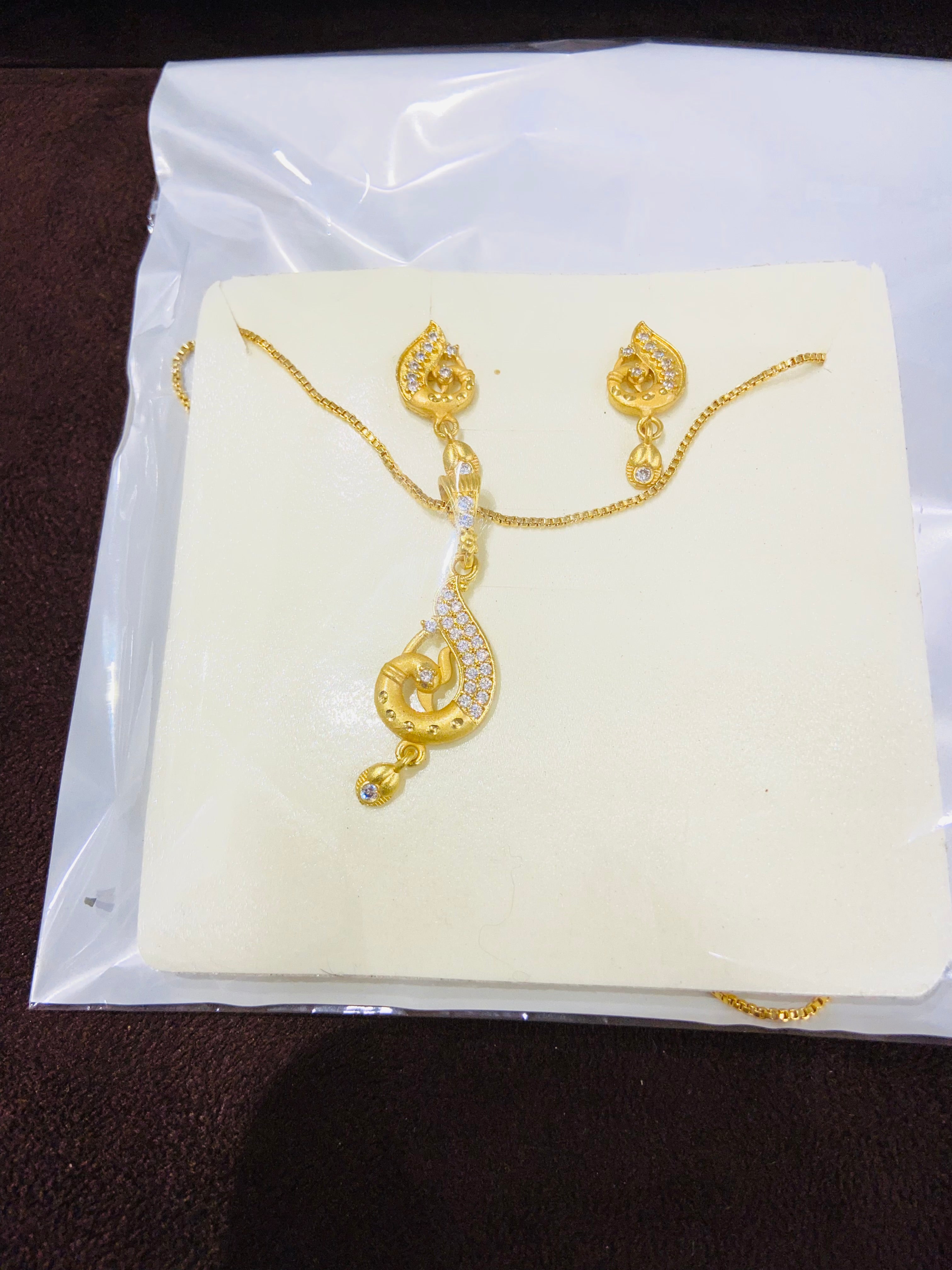 Gold necklace and earrings on a white card with a clear plastic cover