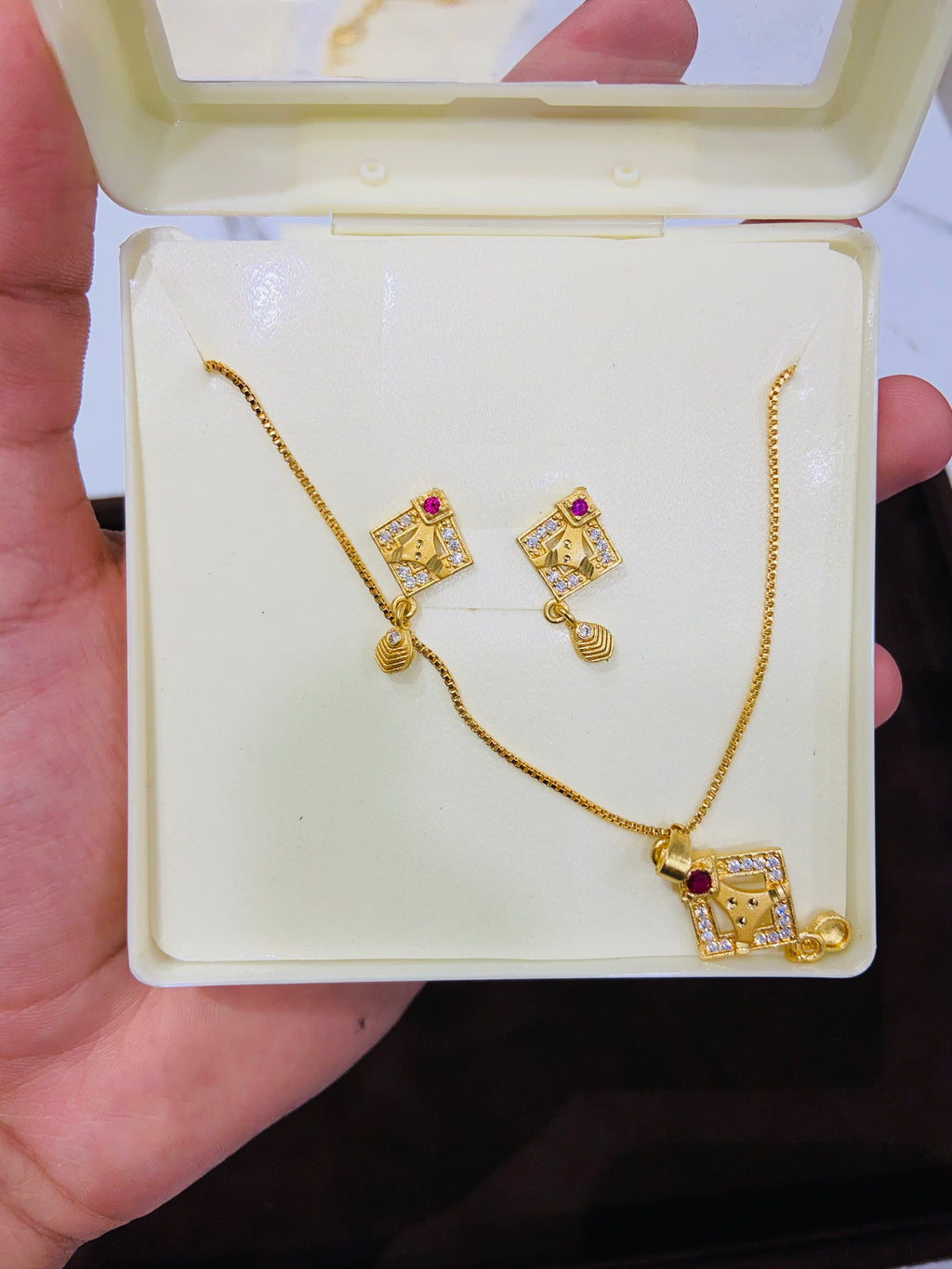 Gold necklace and earrings with red gemstones in a white jewelry box held by a hand.
