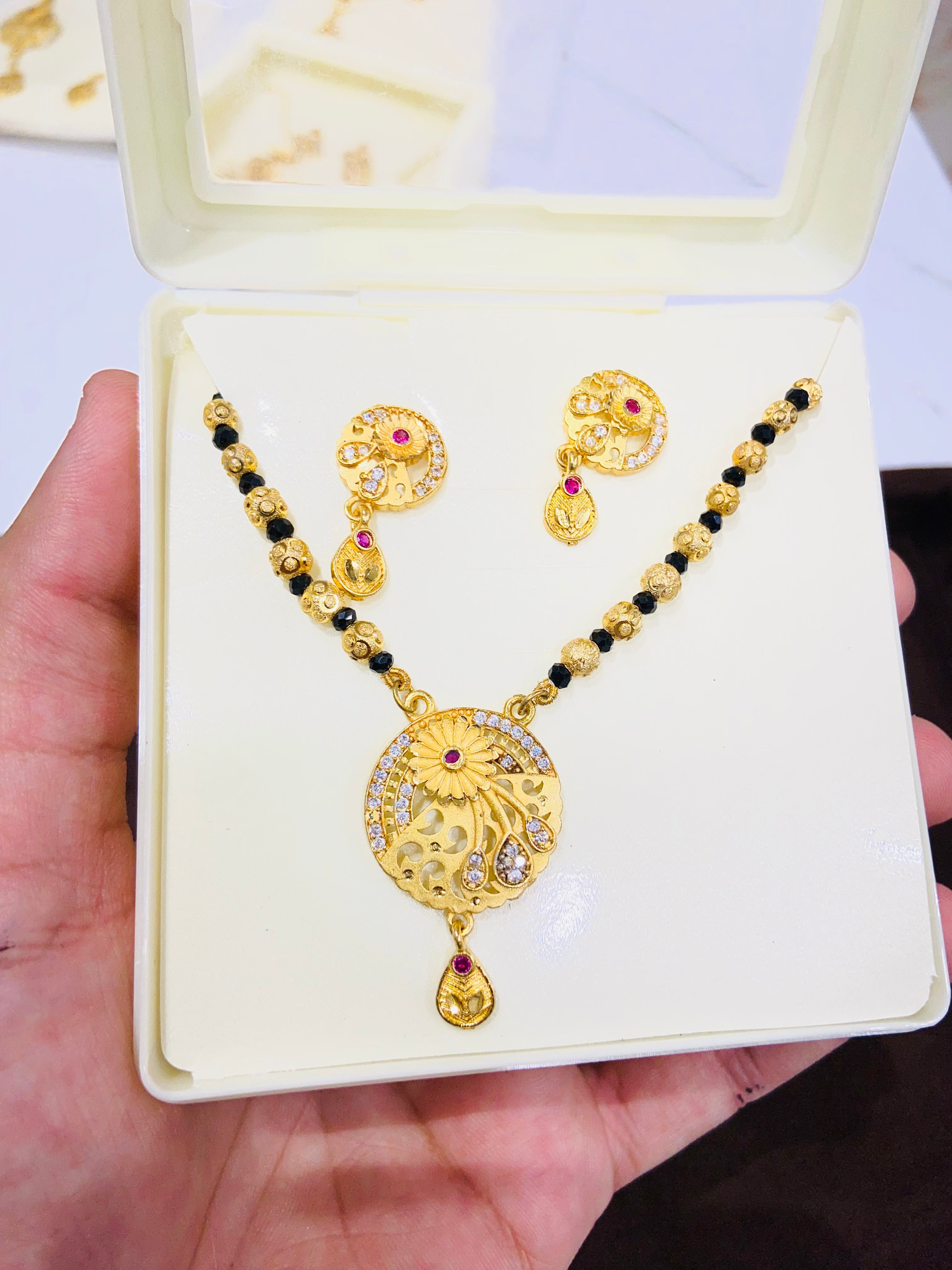 Gold pendant and earrings set on a white display card held in a hand.