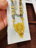 Gold mangalsutra with intricate design on a white card, held by a hand.