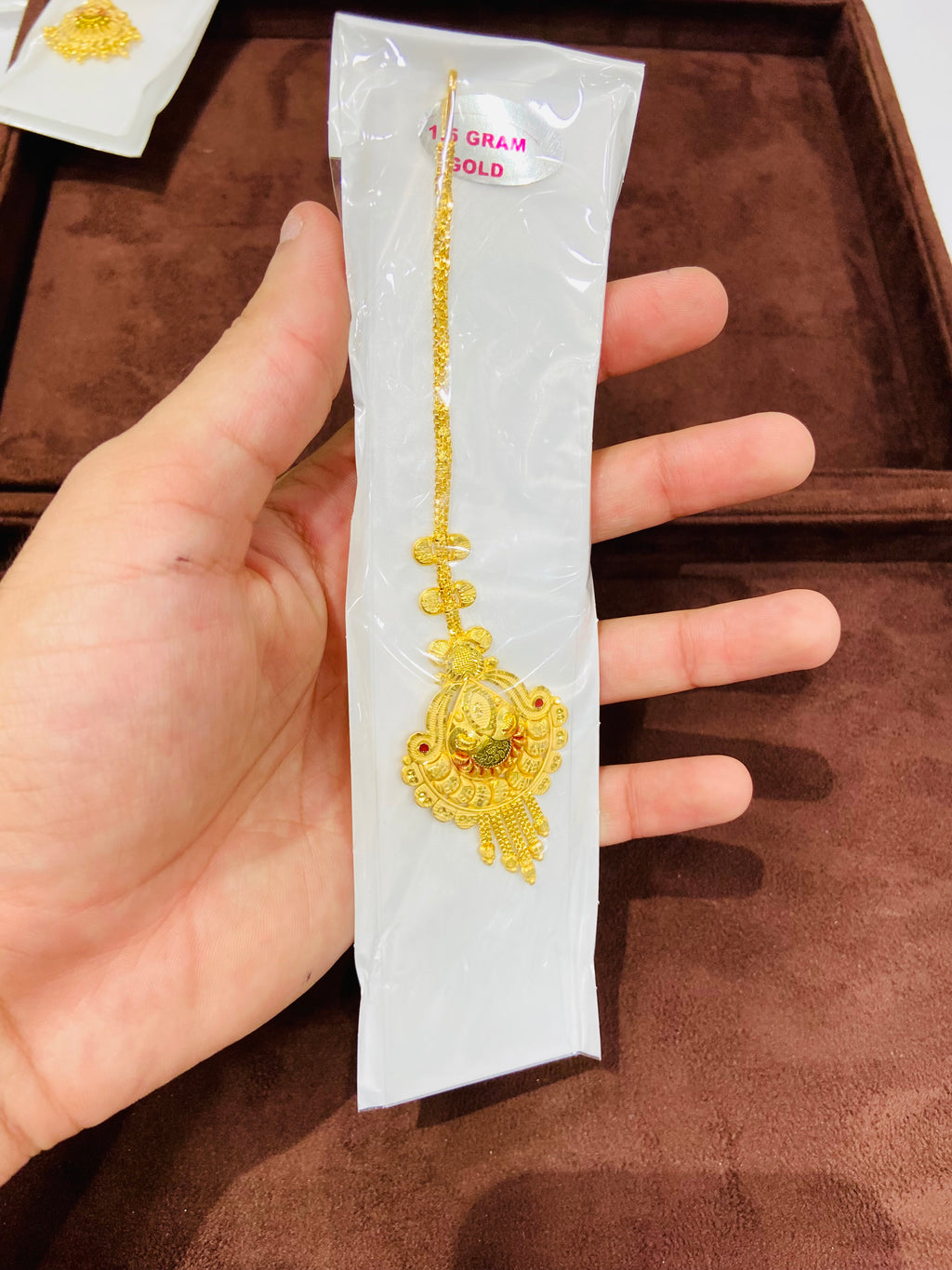 Gold necklace on a white card held by a hand against a brown background