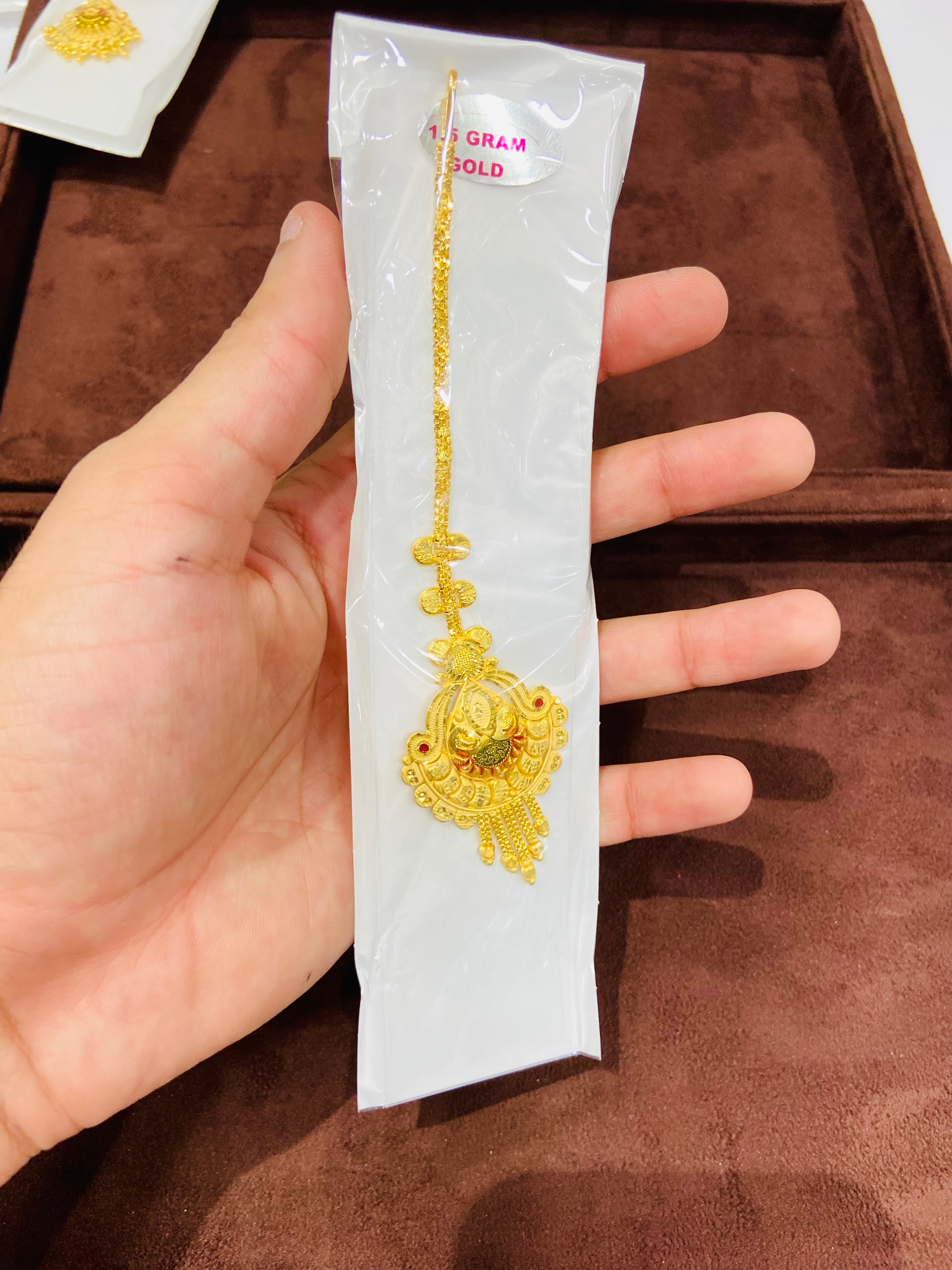 Gold necklace on a white card held by a hand against a brown background