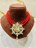 Red beaded necklace with a large decorative pendant on a brown velvet stand.