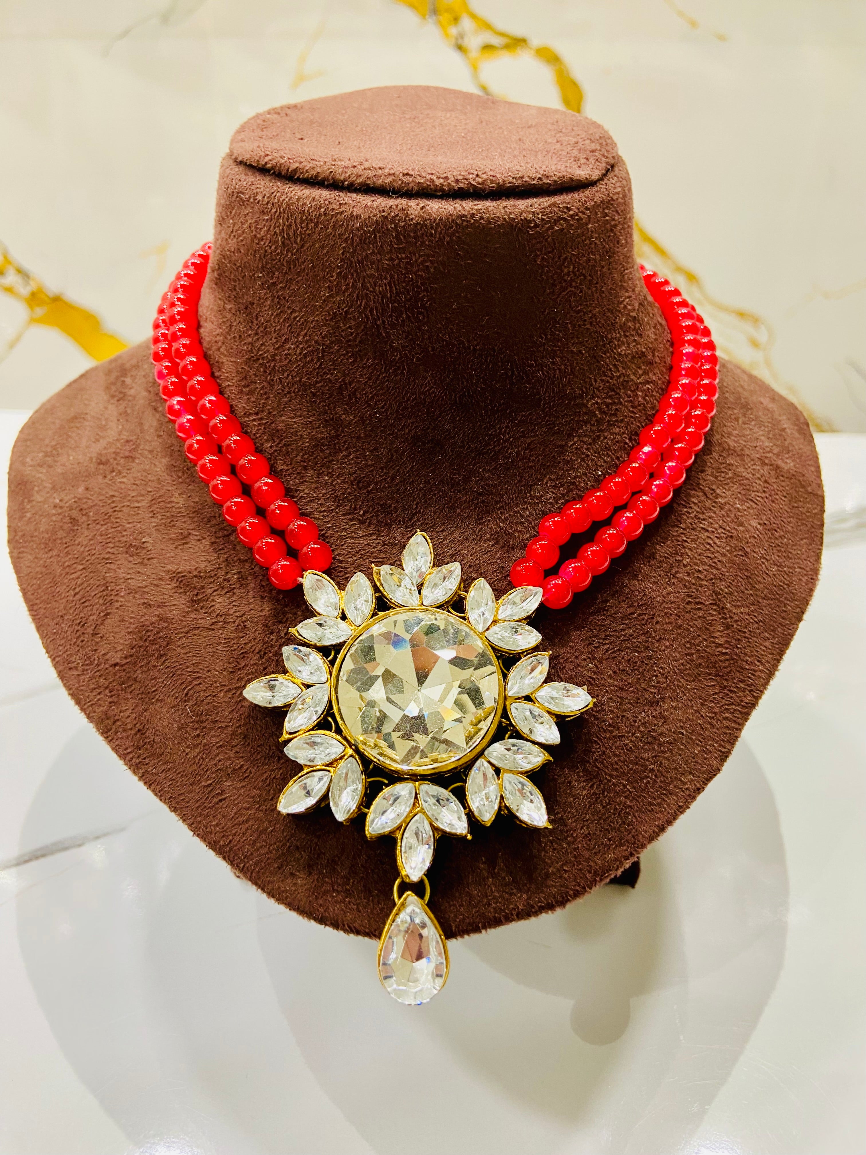 Red beaded necklace with a large decorative pendant on a brown velvet stand.