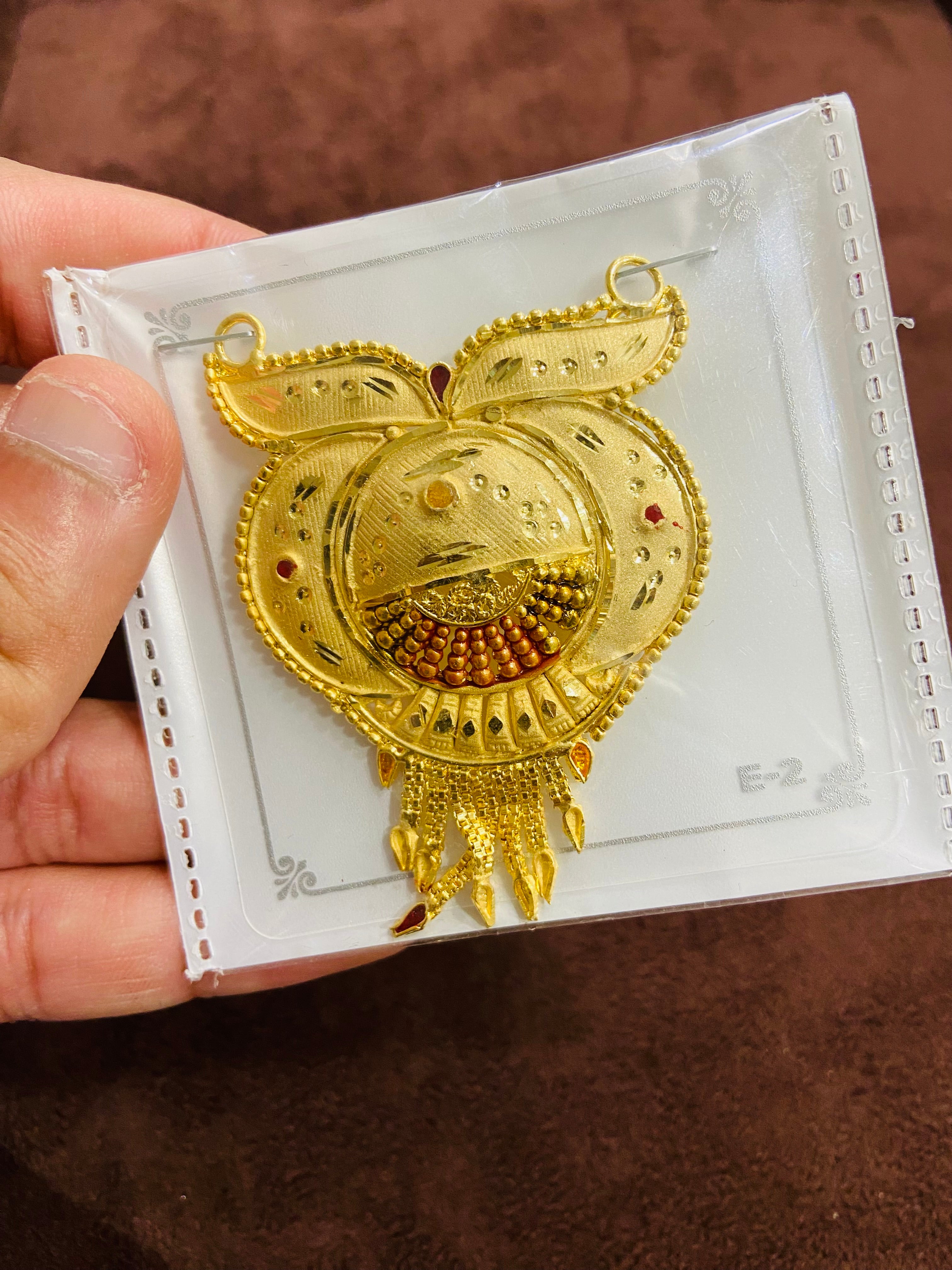 Gold pendant on a white card held by a hand against a brown background