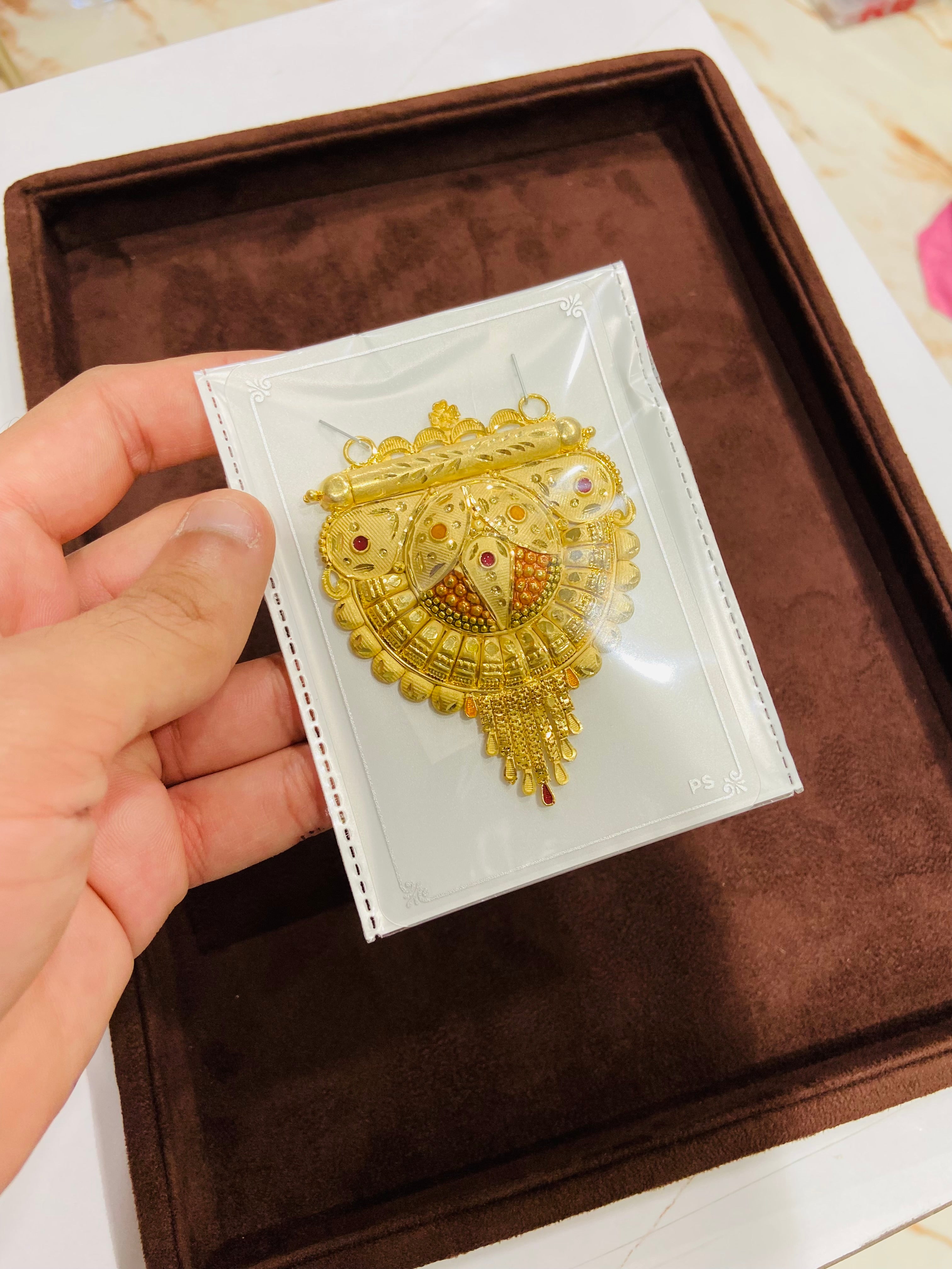 Gold necklace with red stones held over a brown velvet box