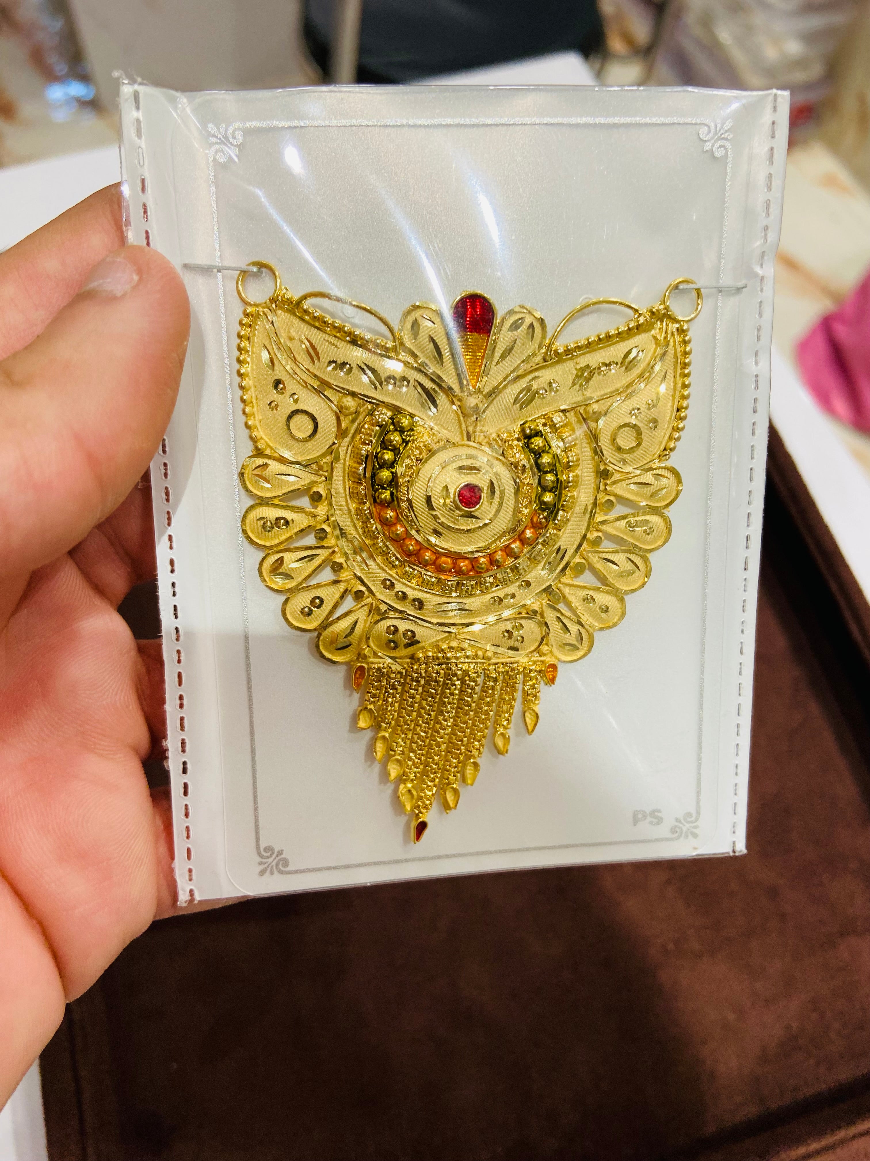 Decorative gold pendant on a white card held by a hand.