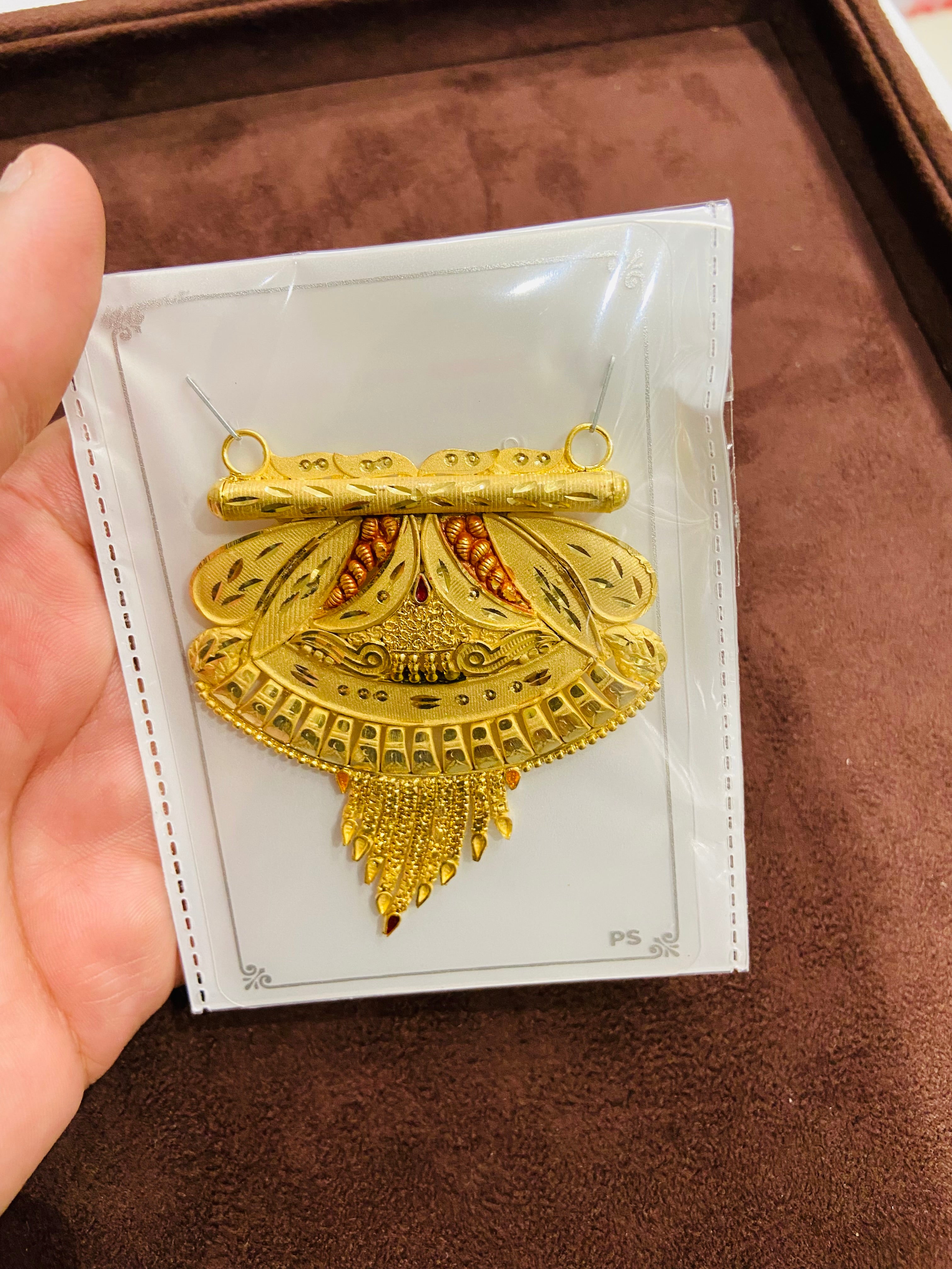 Gold pendant on a white card held by a hand against a brown background