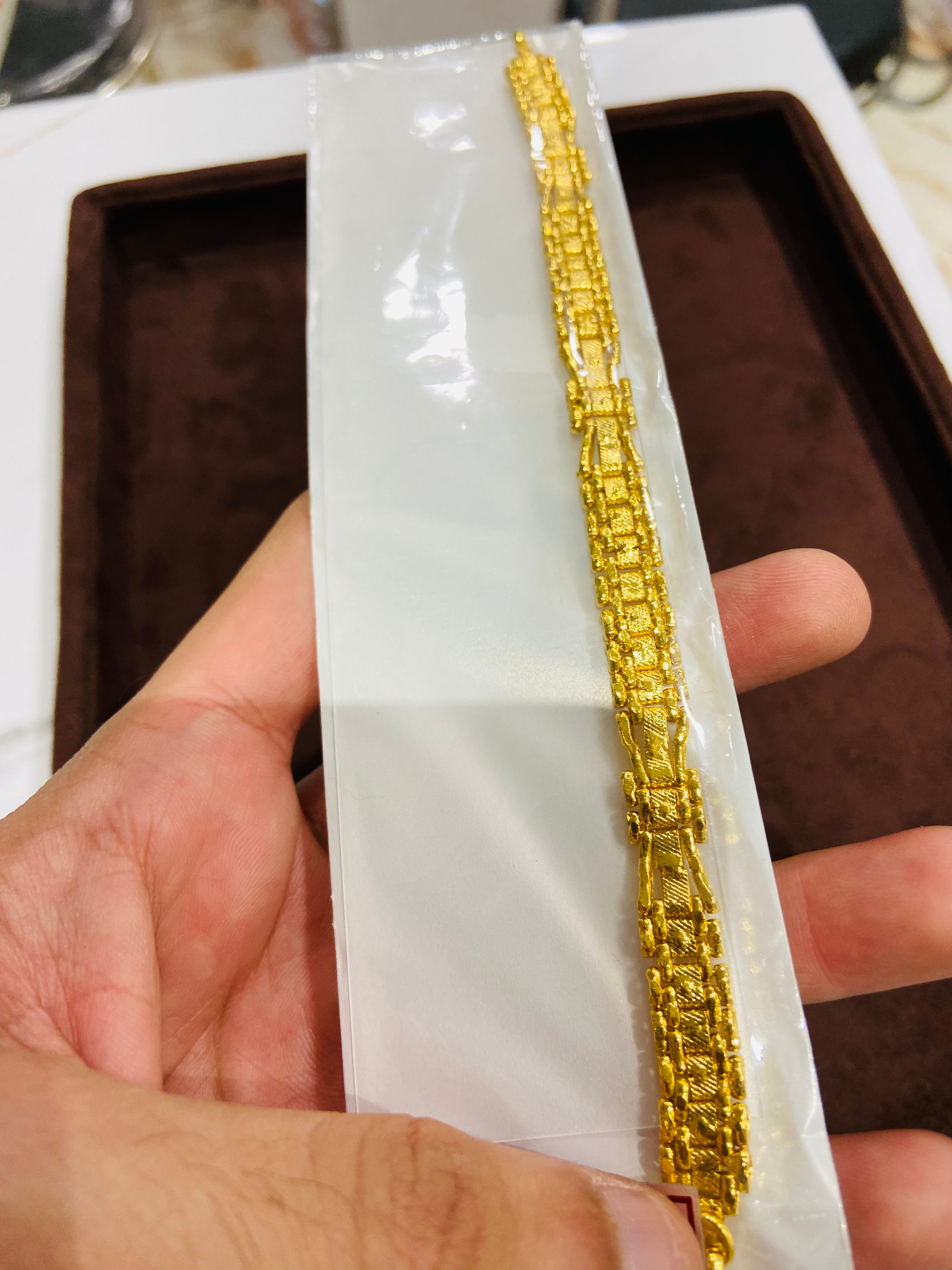 Gold bracelet on a white card held by a hand