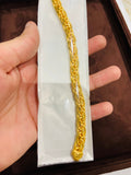 Gold bracelet held by a hand on a white card with a brown background