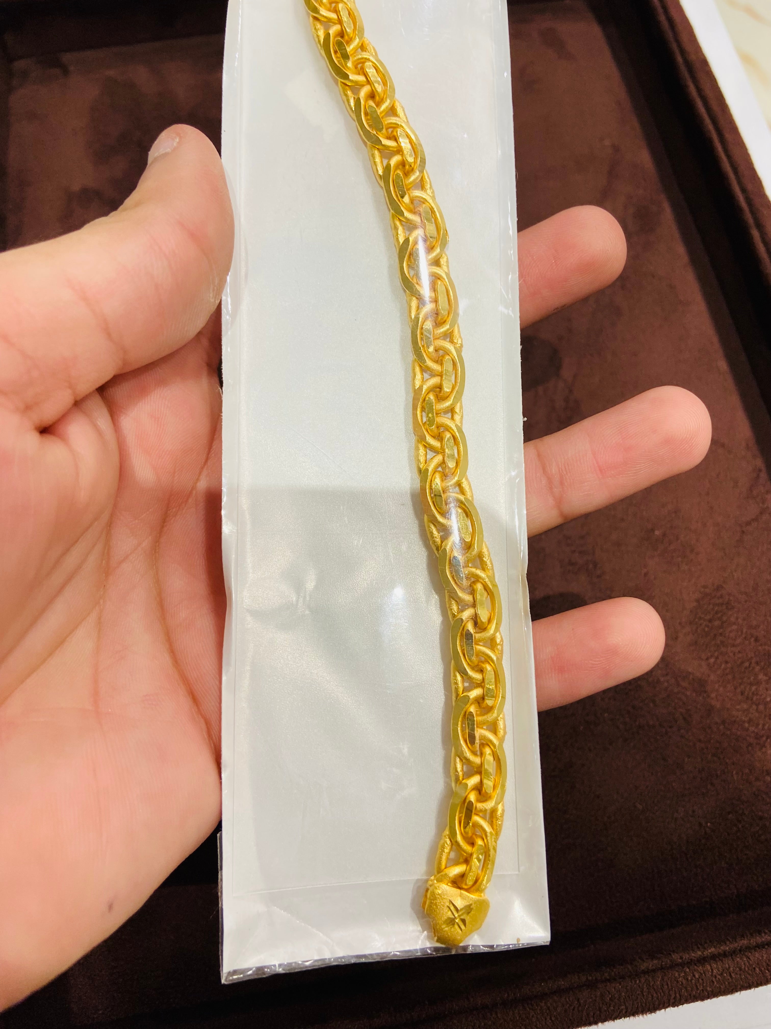 Gold bracelet held by a hand on a white card with a brown background