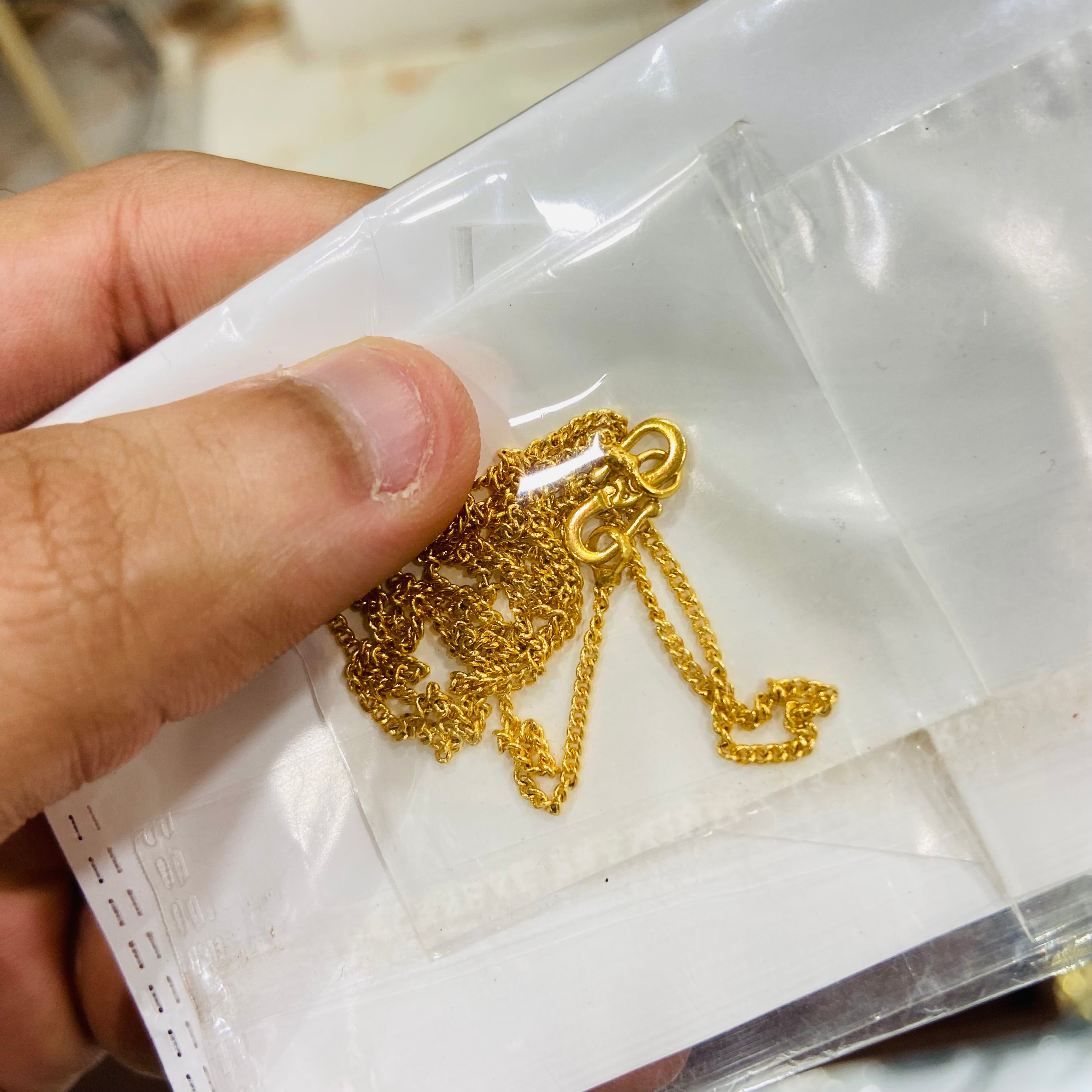 Gold chain held by a hand over a white surface