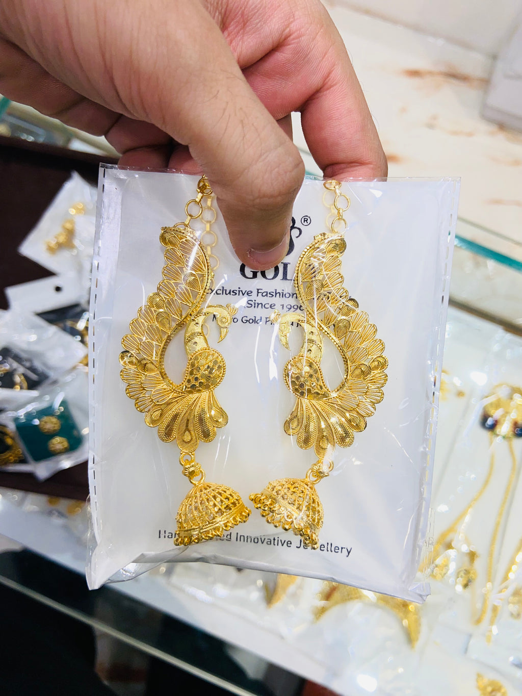 Gold earrings on a display card held by a hand with a blurred background