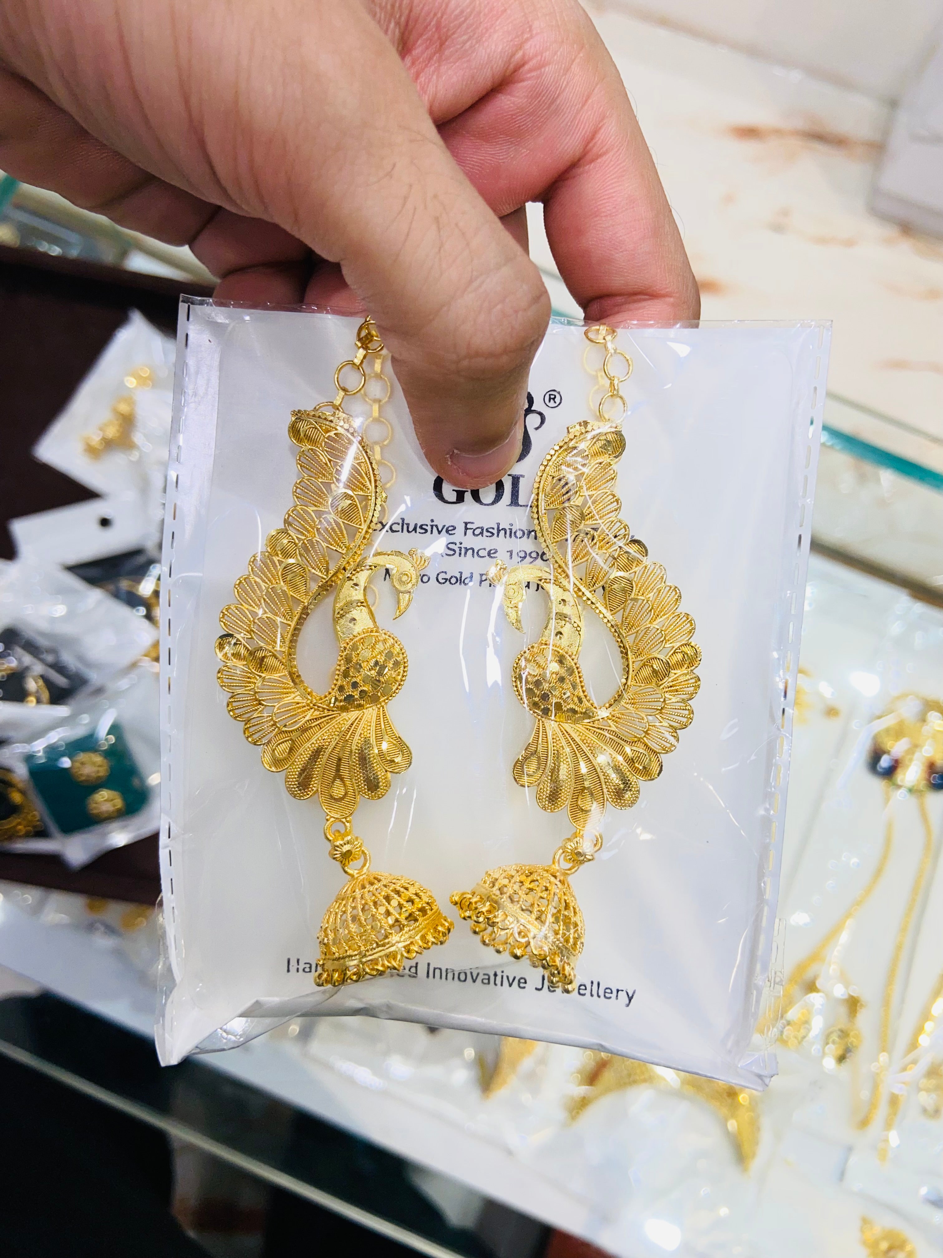Gold earrings on a display card held by a hand with a blurred background