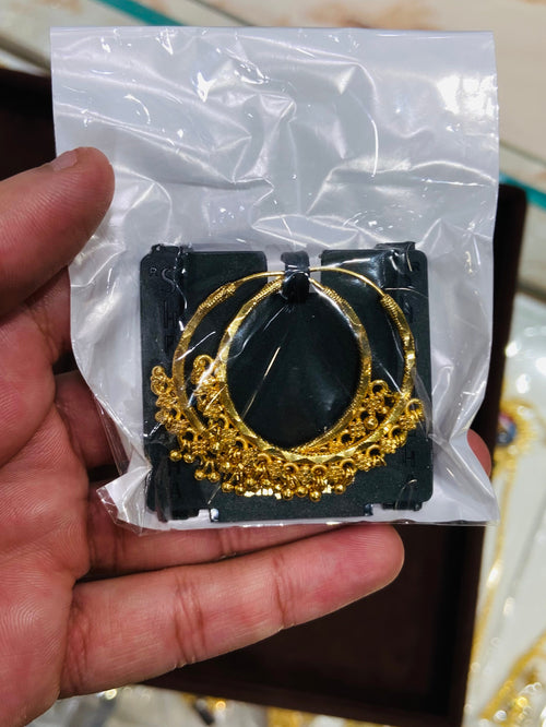 Gold earrings on a white card held by a hand with a reflective surface in the background