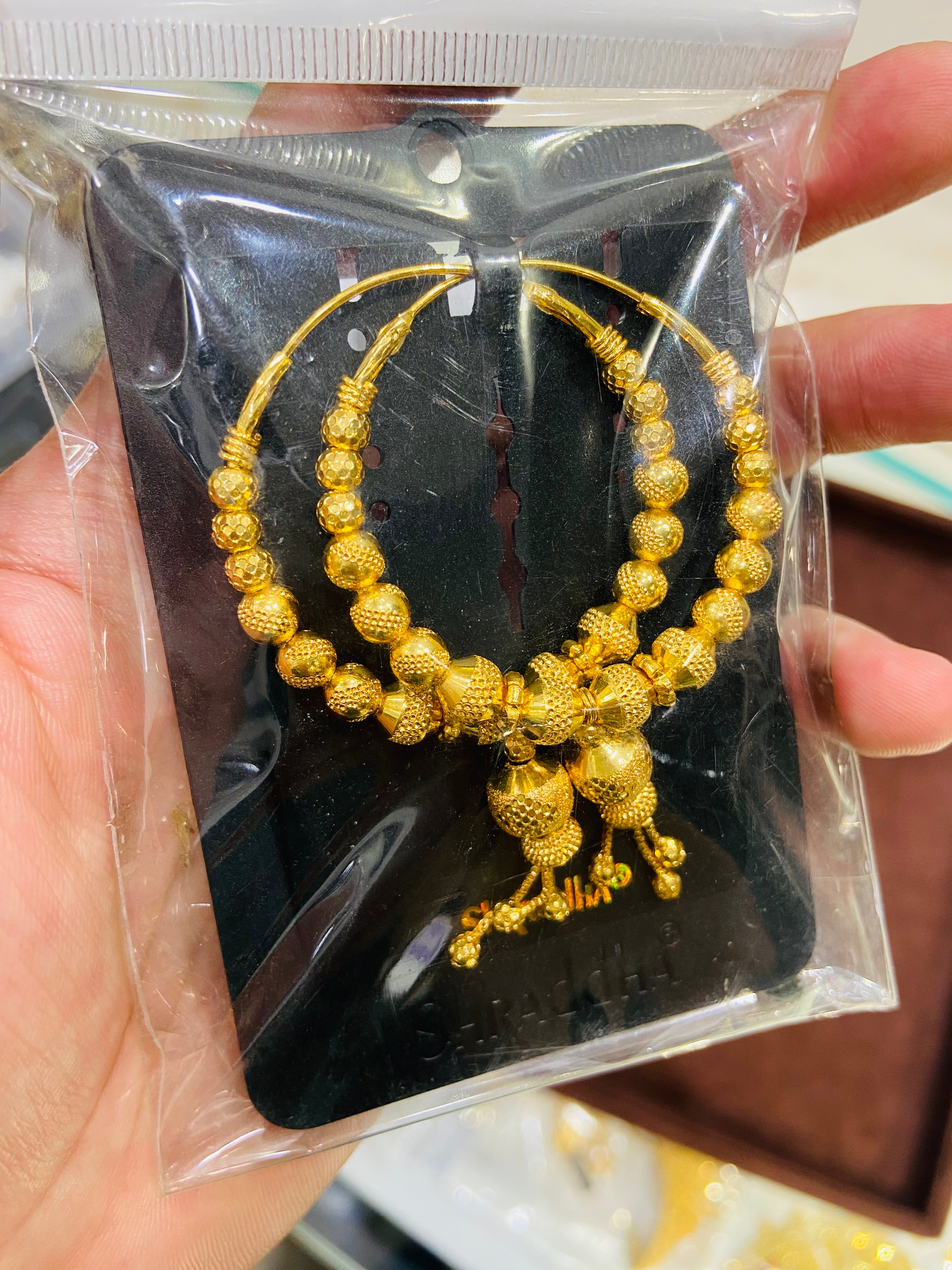 Gold beaded earrings on a clear card held by a hand