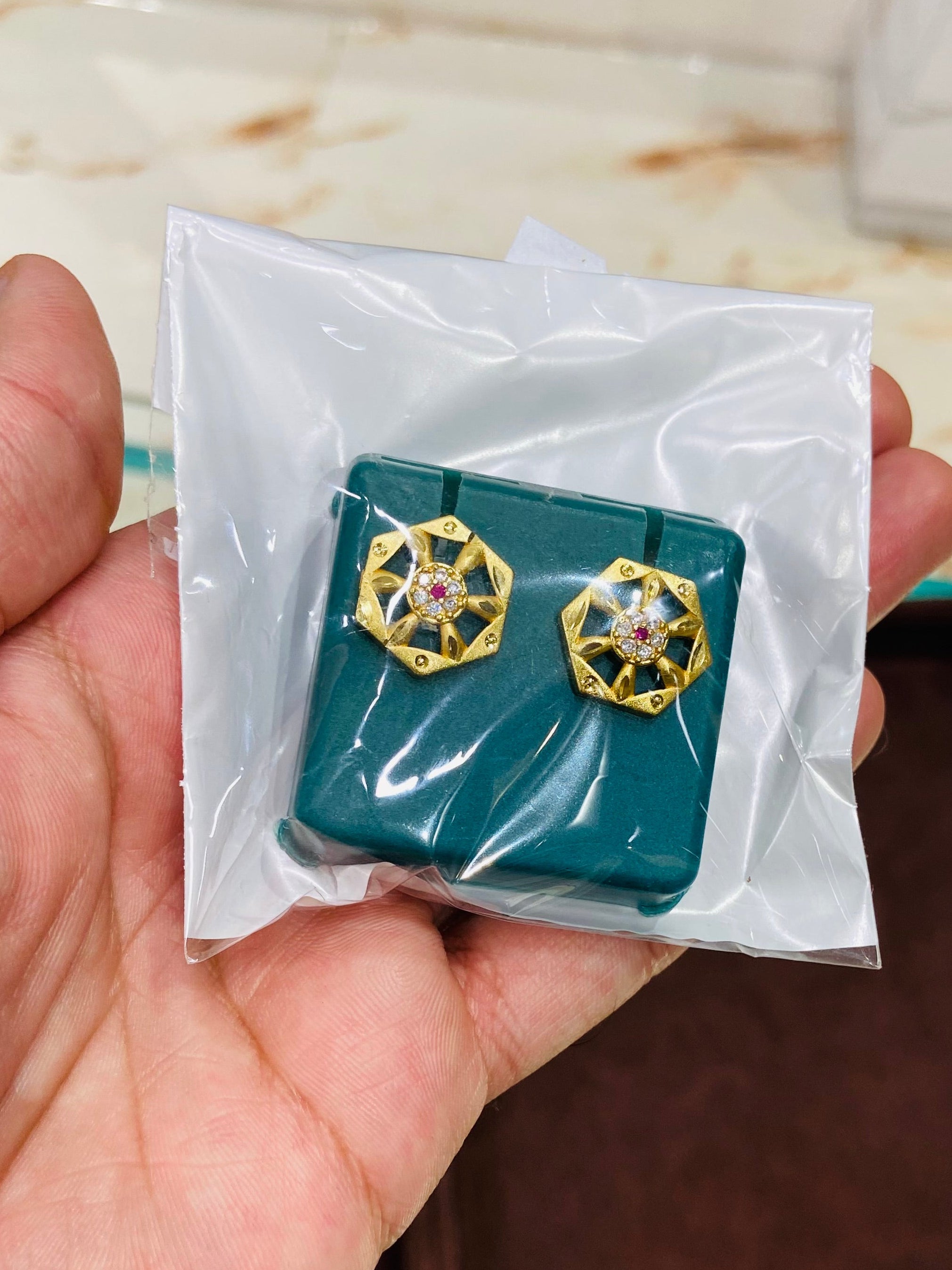 Teal earrings with gold and pink accents held in a hand against a neutral background