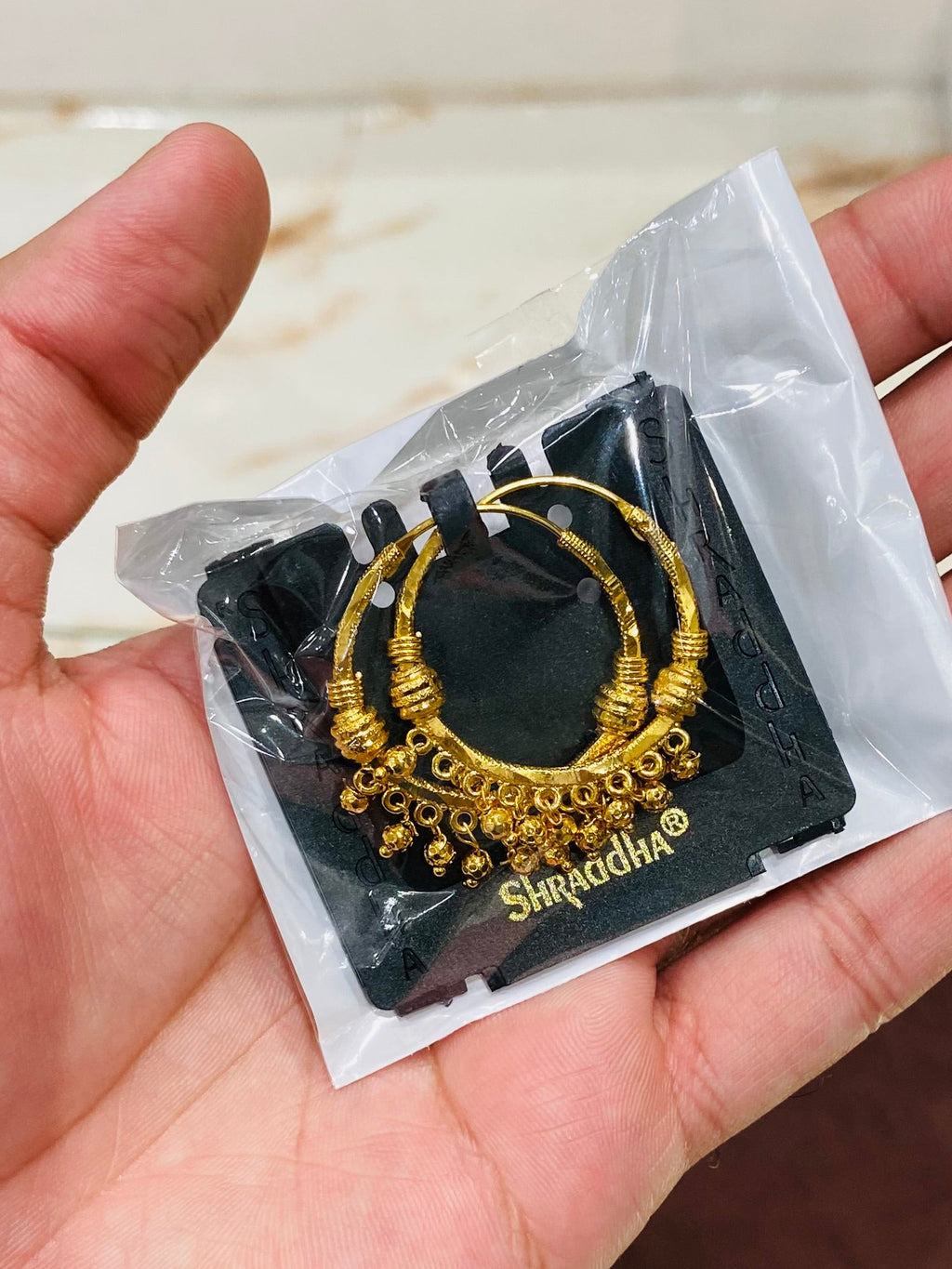 Hand holding a small black card with gold jewelry design on a white background.