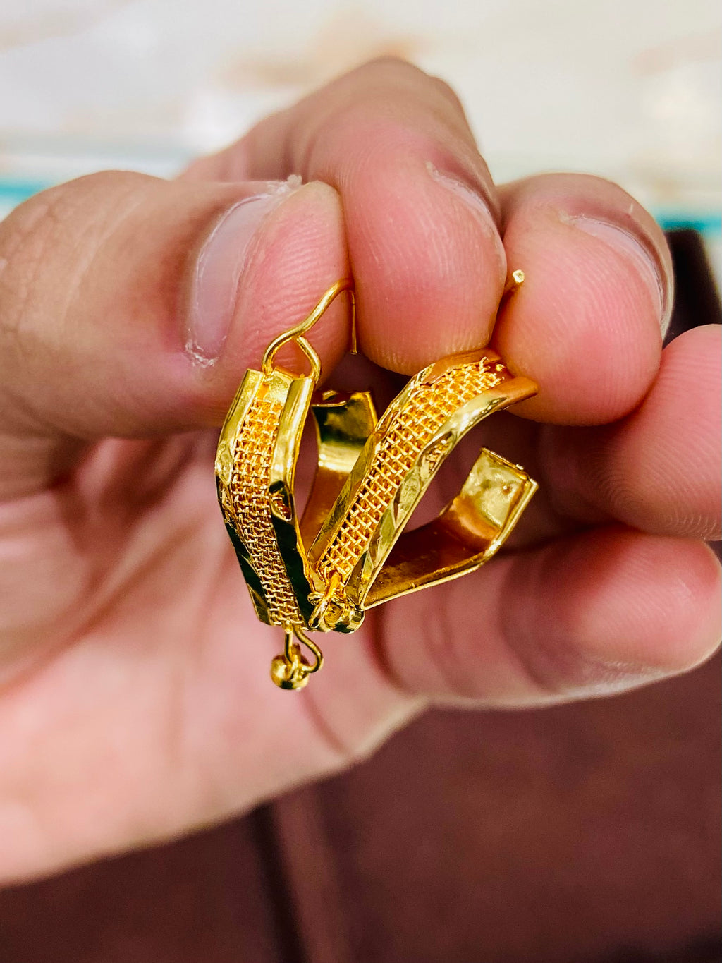 Gold hoop earrings held between fingers against a neutral background