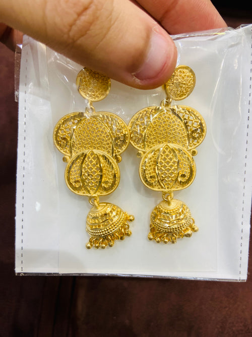 Gold jhumka on a white display card held by a hand.