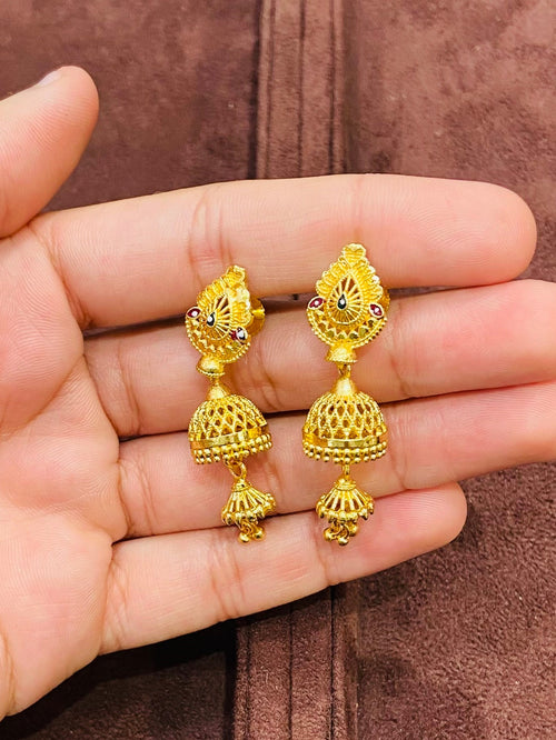 Gold earrings held in a hand with a brown jewelry box in the background